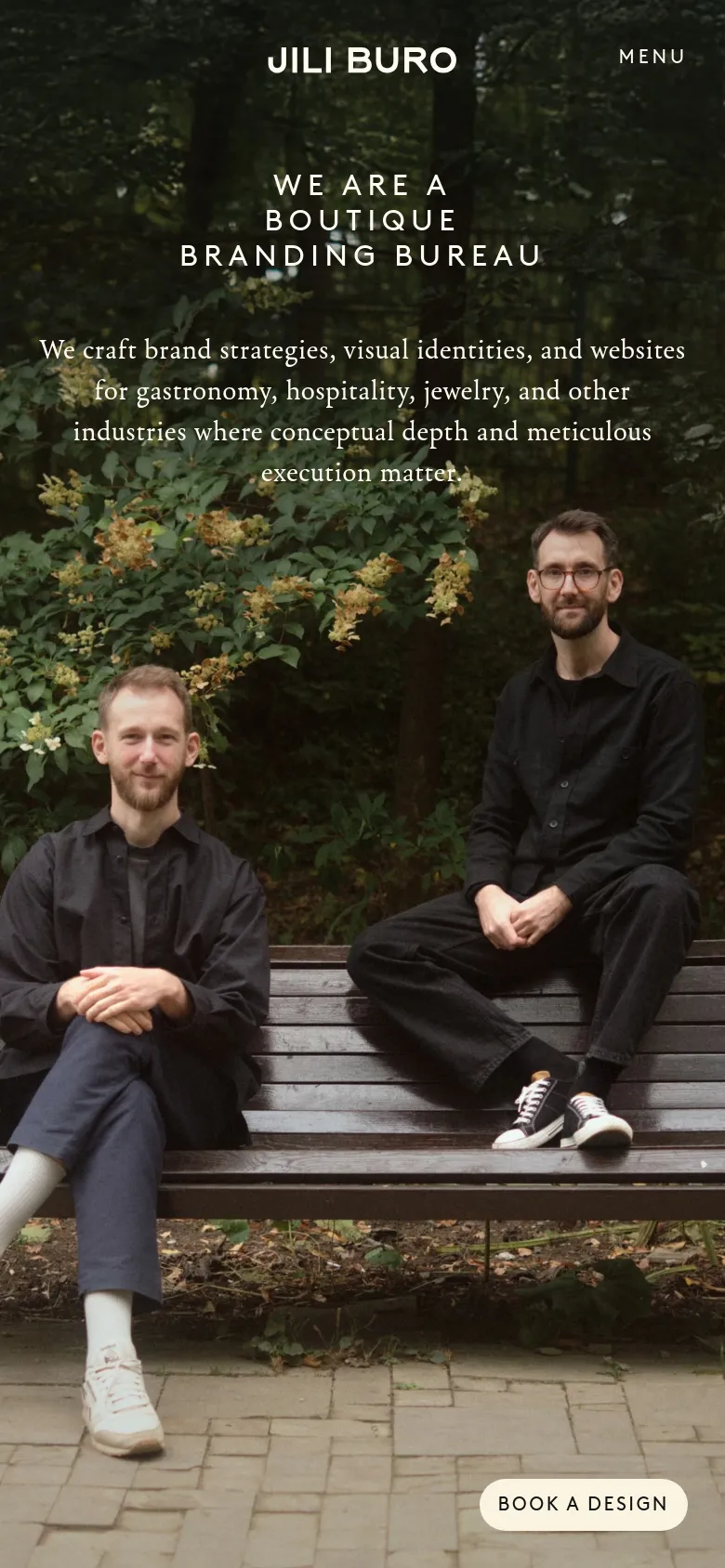 The mobile version presents a vertically stacked layout with the hero image occupying the background. The text is centered, featuring the brand name 'JILI BURO' and a 'MENU' button at the top, followed by the large headline and mission statement. The 'BOOK A DESIGN' call to action is positioned prominently at the bottom right.
