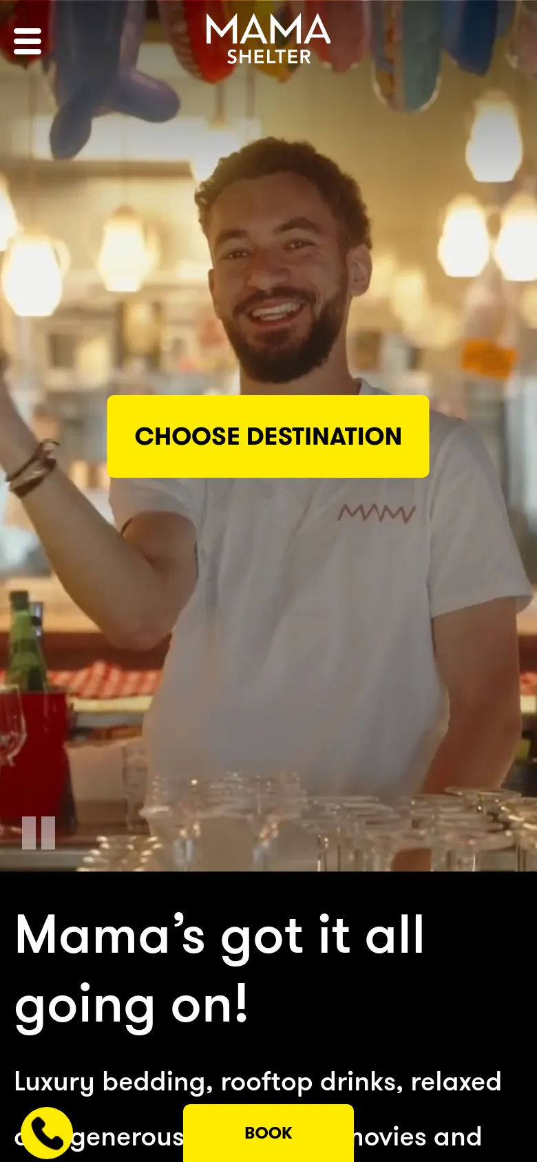 The mobile version shows a full-screen vertical hero image of a smiling man in a restaurant setting, overlaid with a large yellow 'CHOOSE DESTINATION' button. Below the hero section, a black background contains the headline 'Mama’s got it all going on!' in large white text. The navigation is condensed into a hamburger menu icon in the top left, and a yellow 'BOOK' button is fixed at the bottom.