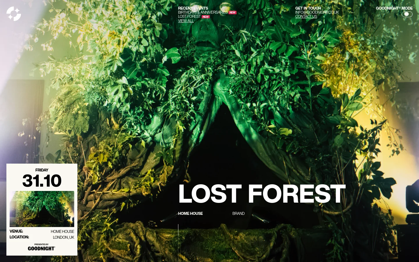 Goodnight Lost Forest event page featuring a full-bleed hero image of a lush, dark green forest installation with a mystical Green Man figure. Large white sans-serif typography displays the event title, date, and venue details over the immersive botanical decor. The layout uses a sophisticated dark aesthetic with high-contrast text and a minimalist navigation bar.