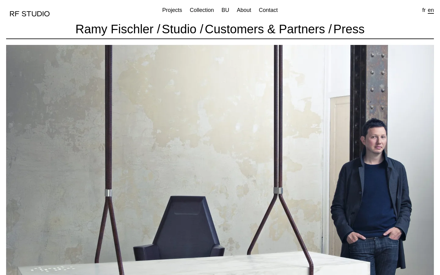 The desktop version features a minimalist white layout with a top navigation menu containing links like Projects and About. A large hero image shows designer Ramy Fischler standing in a modern interior next to a marble table and sculptural tripod legs, followed by a large headline and biographical text.