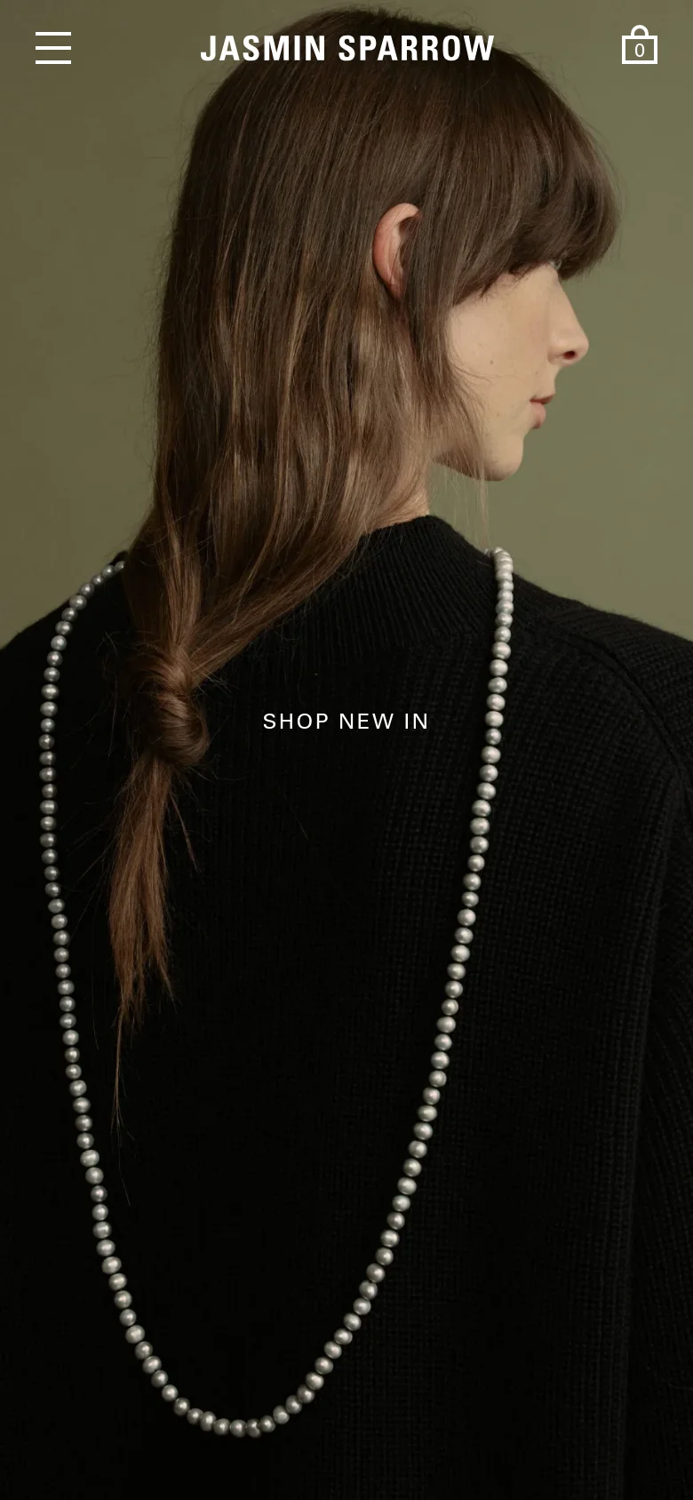The mobile version simplifies the layout, displaying a full-width hero image of a woman in a black sweater wearing a pearl necklace. The top navigation is condensed into a hamburger menu icon on the left, the brand name 'JASMIN SPARROW' is centered, and a shopping cart icon is on the right. The 'SHOP NEW IN' call to action is centered over the portrait image.