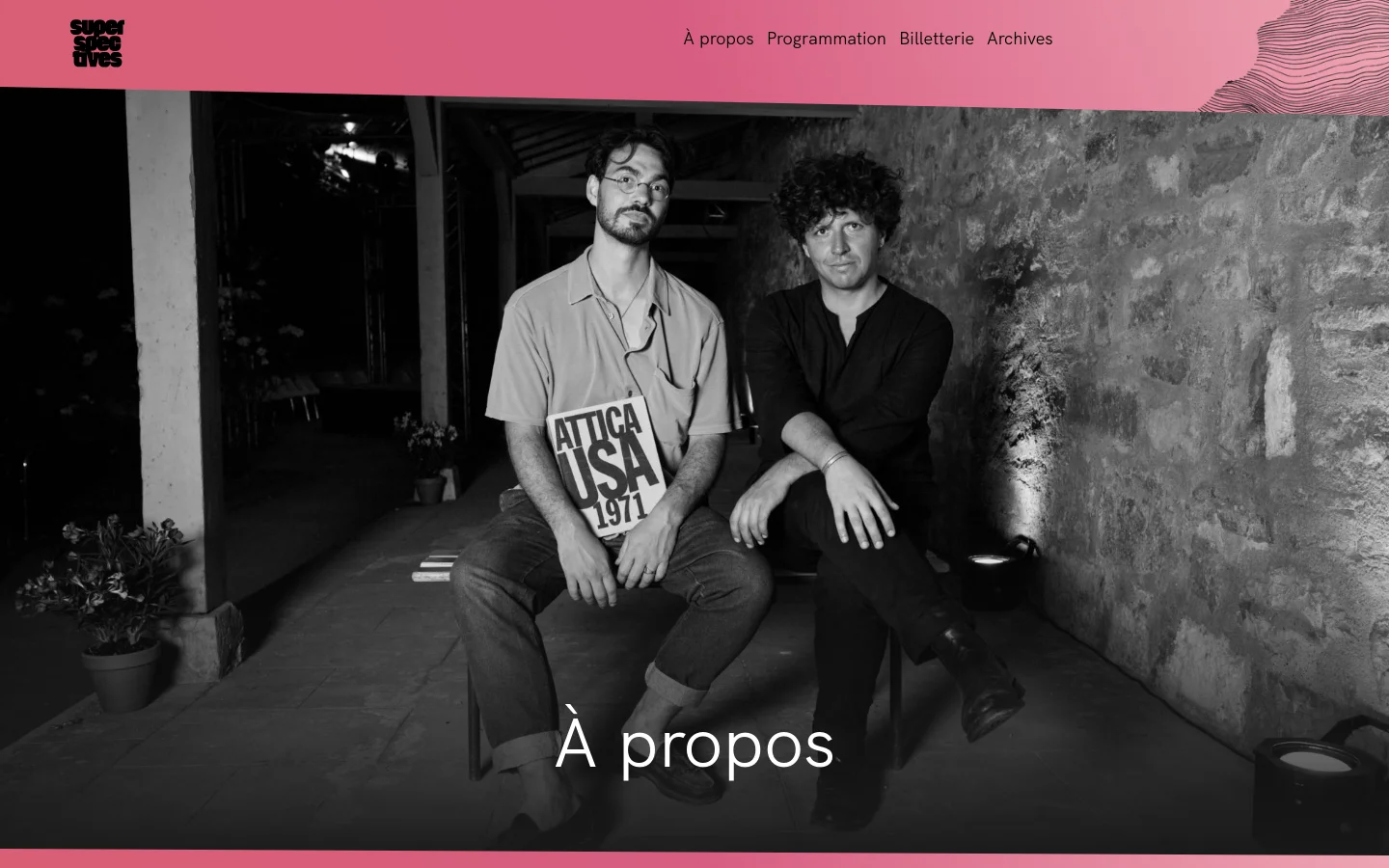 The desktop page features a pink header with the Superspectives logo on the left and a navigation menu on the right. Below, a large black and white photograph shows two men sitting in an outdoor courtyard, with the large white headline 'À propos' overlaid at the bottom.
