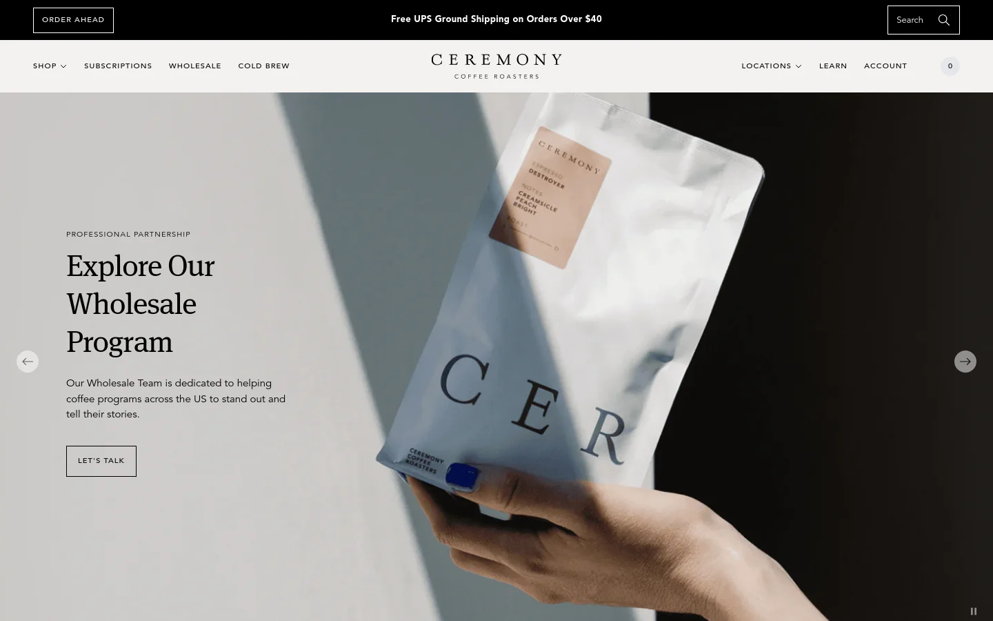 The desktop homepage features a large hero slider with a hand holding a bag of Ceremony coffee against a minimalist background. Below the hero, a white content section contains the headline 'Explore Our Wholesale Program' and a 'LET'S TALK' call-to-action button. The navigation bar is clean with links for Shop, Subscriptions, Wholesale, and Cold Brew, set against a white background with a black announcement bar at the top.