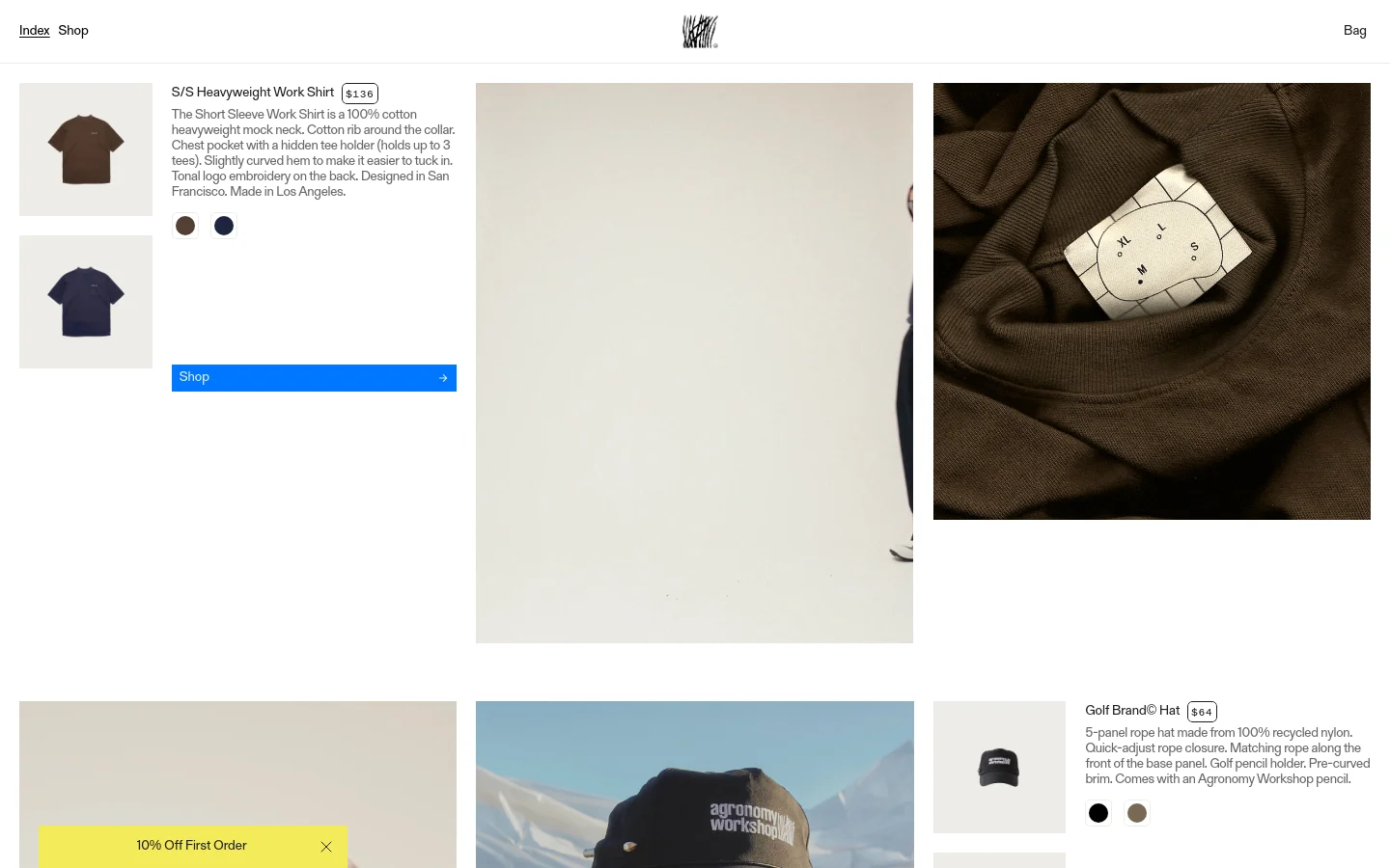 The desktop homepage features a minimalist design with a light beige background and a clean navigation bar containing 'Index', 'Shop', and 'Bag'. The layout showcases product sections with large lifestyle imagery, including a person wearing a dark navy shirt and wide-leg trousers, alongside product shots and descriptions for the S/S Heavyweight Work Shirt and Golf Brand Hat.