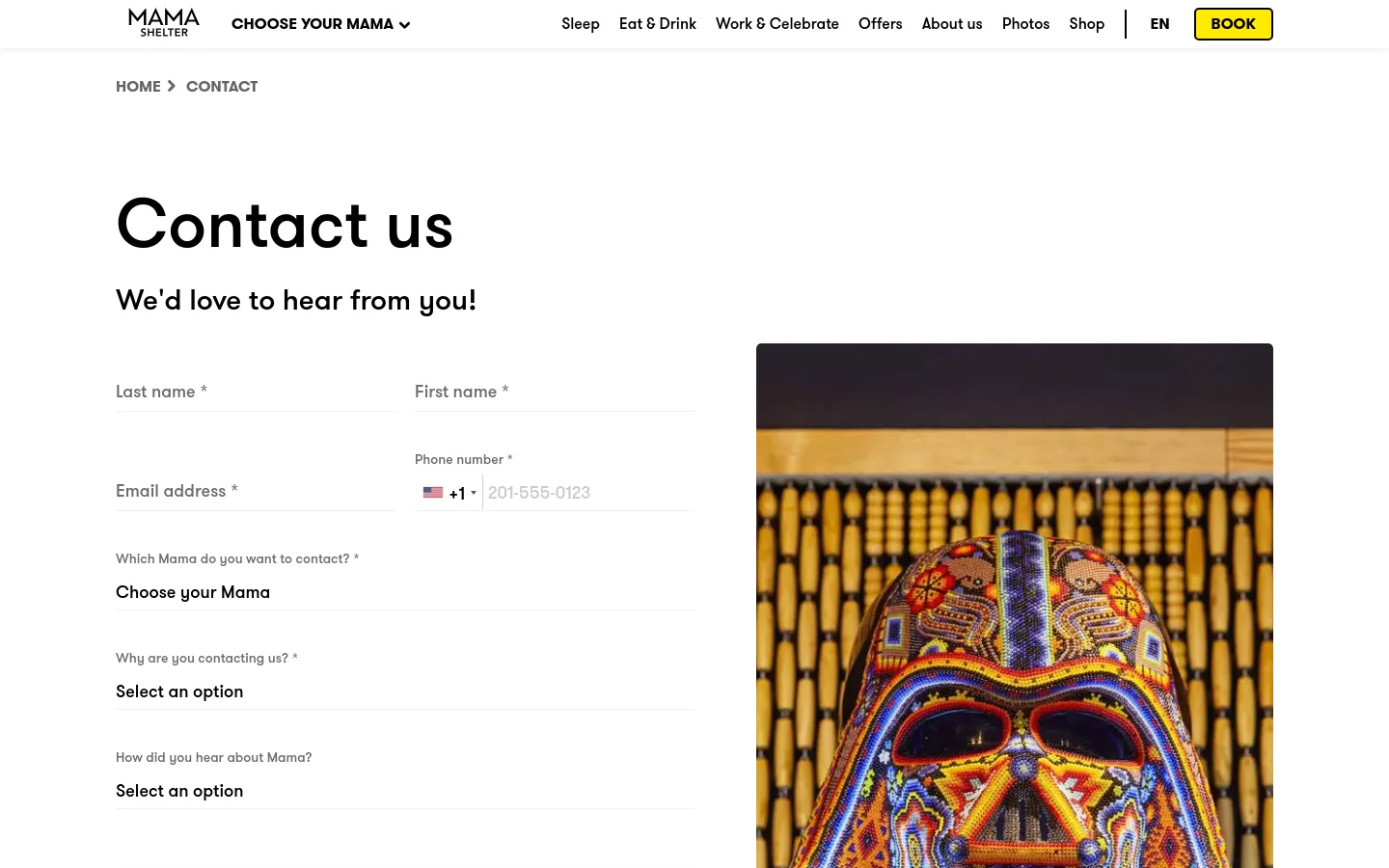The desktop Contact page features a large 'Contact us' headline with a subheadline 'We'd love to hear from you!' on the left. A multi-field contact form is positioned on the left side, while a large, colorful vertical image of a decorative mask occupies the right side. The navigation bar at the top is white with black text and a yellow 'BOOK' button.