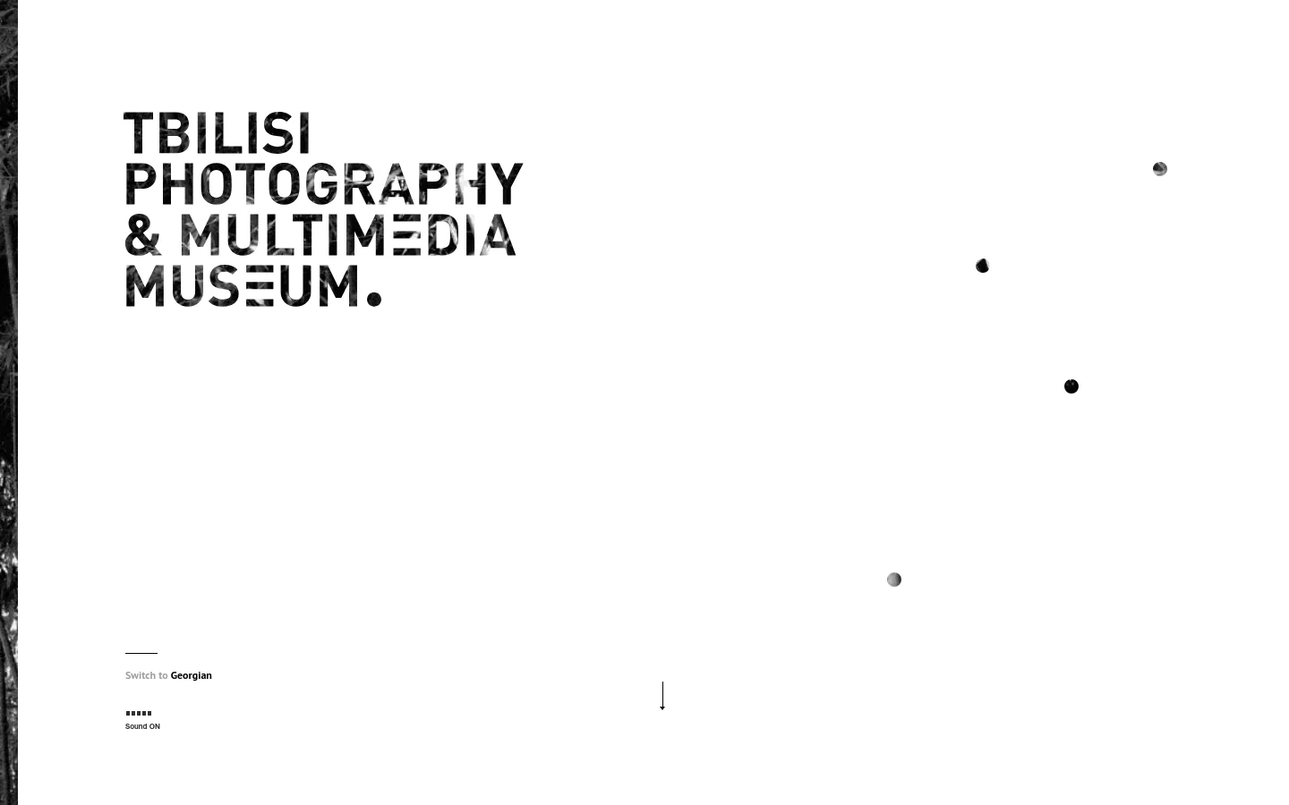 The desktop homepage features a minimalist design with large, bold black typography reading 'TBILISI PHOTOGRAPHY & MULTIMEDIA MUSEUM' against a white background. Small dark circular elements float in the white space, and a navigation menu is accessible via text links. A 'Switch to Georgian' option and a 'Sound ON' indicator are visible in the lower-left area.