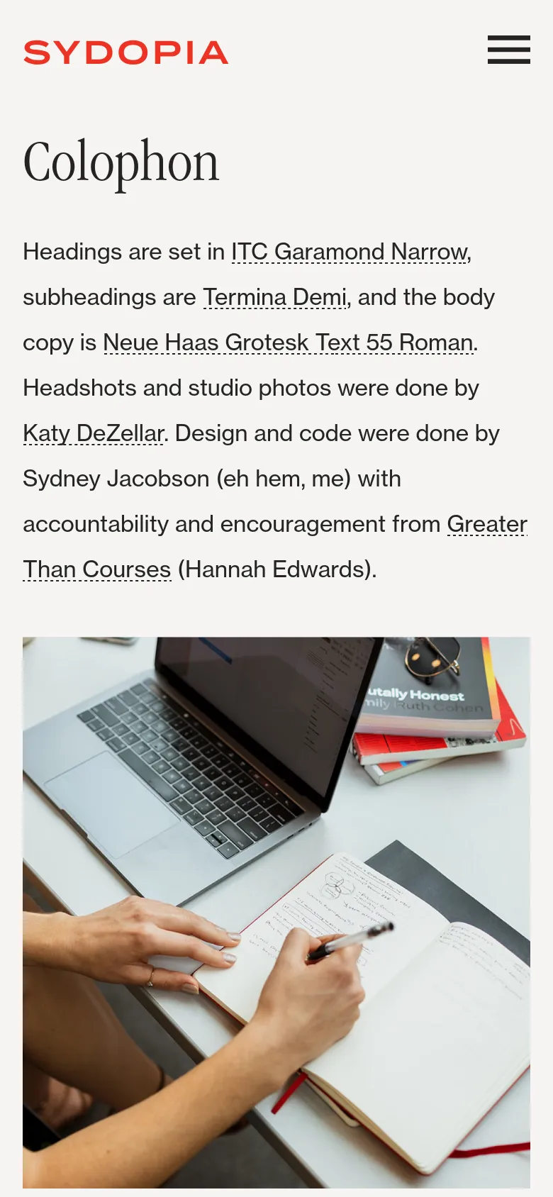 The mobile version uses a single-column layout with the red Sydopia logo centered at the top and a hamburger menu icon on the right. The 'Colophon' heading and text are positioned above a large, full-width photograph of a person writing in a notebook next to a laptop.