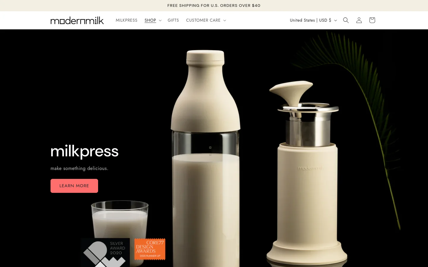 The desktop homepage features a dark, minimalist aesthetic with a large hero image of a cream-colored milkpress bottle and glass against a black background. A white headline reads 'milkpress' followed by 'make something delicious' and a peach-colored 'LEARN MORE' button. The layout uses full-width high-quality photography to showcase various plant-based milk products and tools.