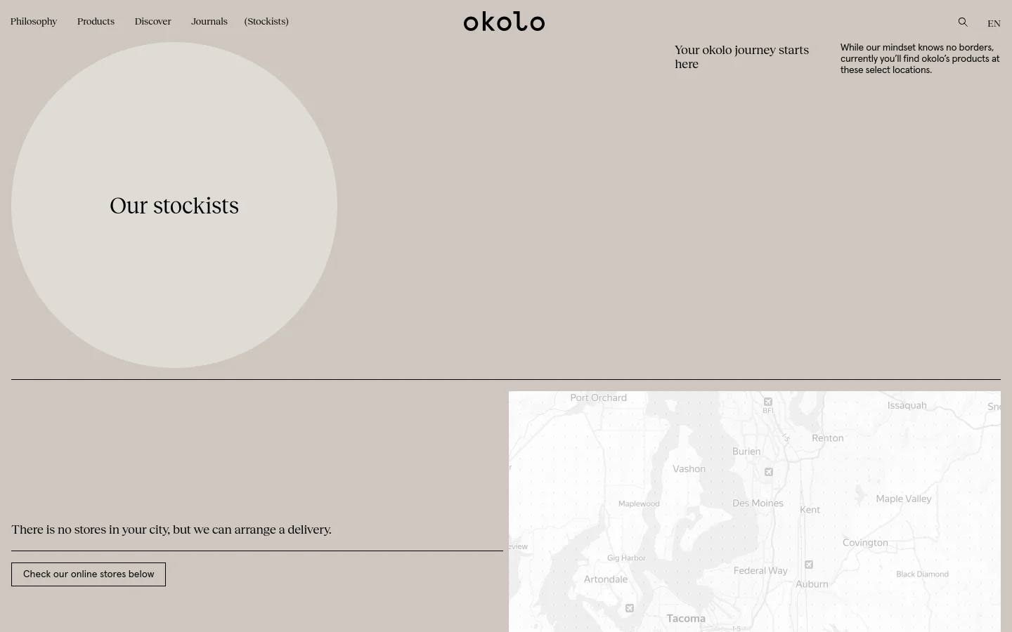 The desktop page features a minimalist design with a neutral beige and cream color palette. A large, off-white circle contains the headline 'Our stockists' against a light background, followed by a section with a map and text stating that products are available at select locations. Navigation links are at the top, and a 'Check our online stores below' button is positioned on the left.