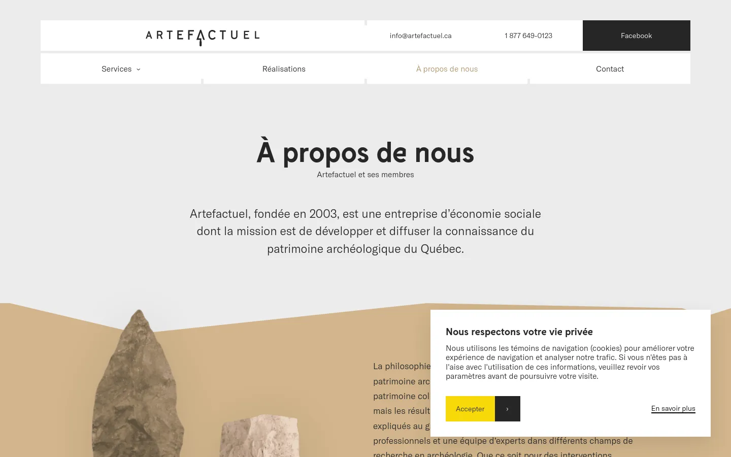 The desktop page features a clean, minimalist design with a light gray background and a white navigation bar at the top containing links for Services, Réalisations, À propos de nous, and Contact. The hero section displays a large, centered headline 'À propos de nous' followed by a subheadline and a brief introductory paragraph about Artefactuel. A large, out-of-focus image of a stone artifact is visible in the lower-left corner, partially covered by a cookie consent pop-up.