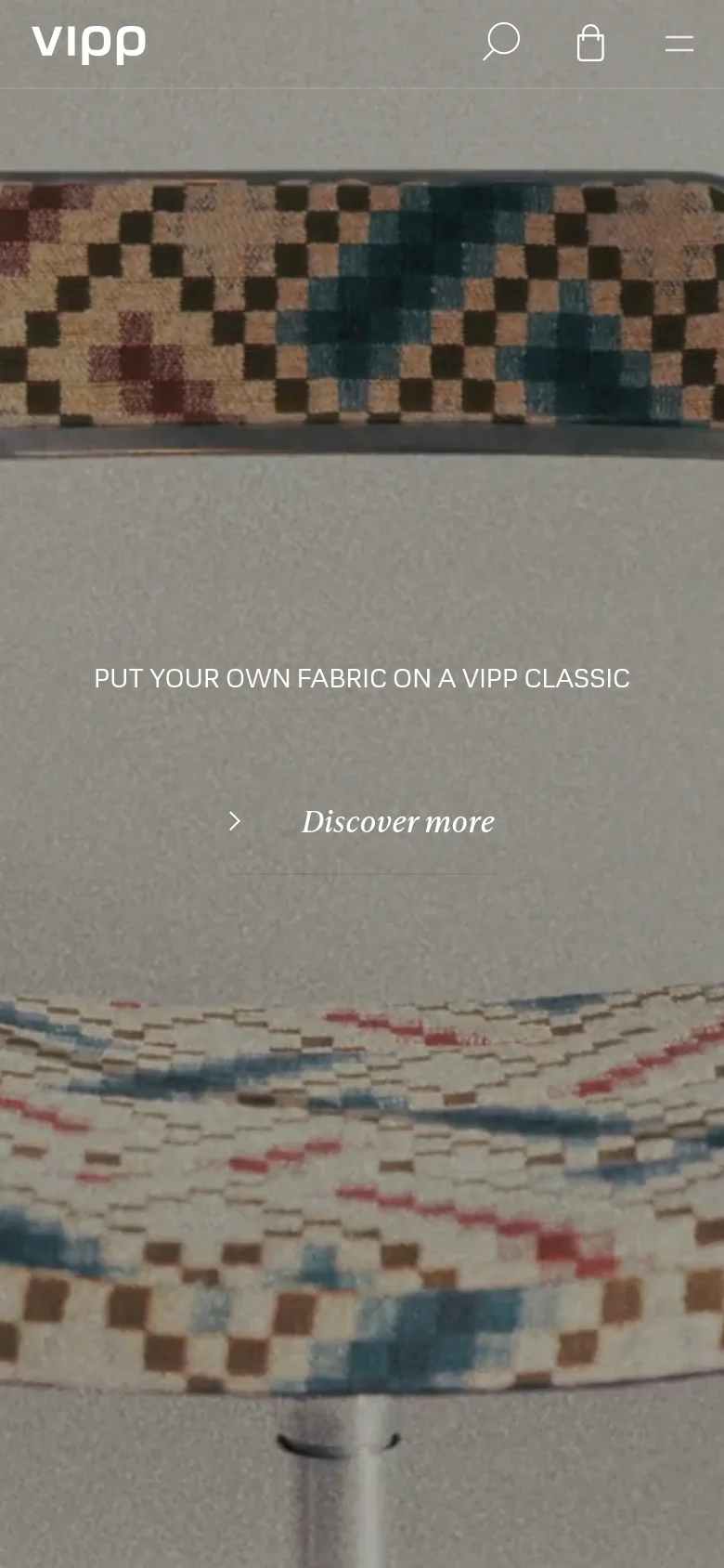 The mobile version presents a vertically oriented view of the hero image, focusing on the patterned fabric of the furniture. The headline 'PUT YOUR OWN FABRIC ON A VIPP CLASSIC' and 'Discover more' link are centered on the screen. The top navigation is condensed into a hamburger menu icon next to the brand logo, a search icon, and a shopping bag icon.