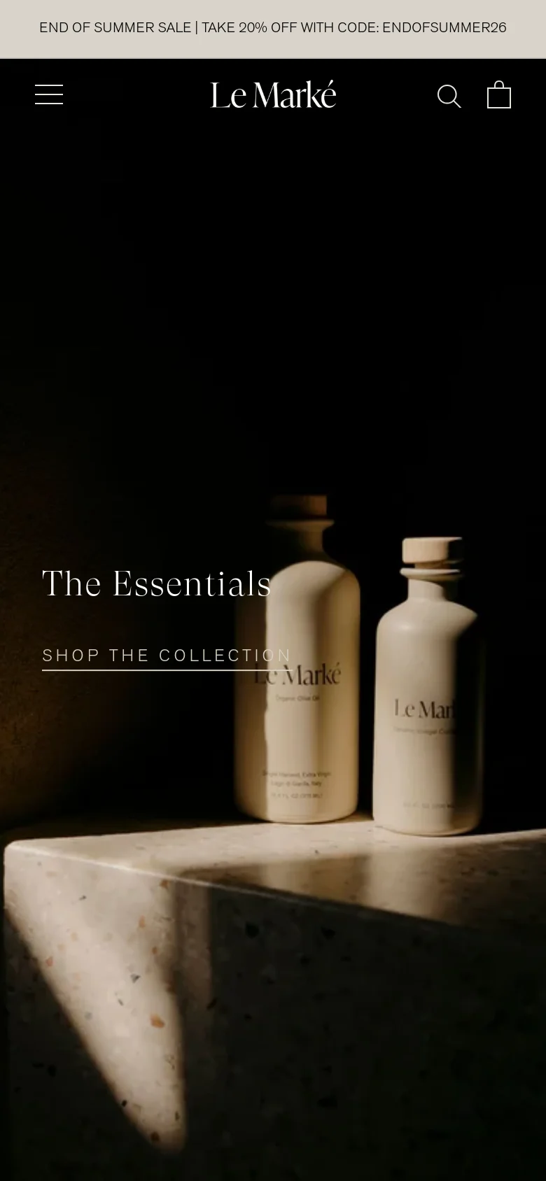 The mobile version uses a simplified layout with a centered logo and a hamburger menu icon on the left. The hero image remains the focal point, with the 'The Essentials' headline and 'Shop the Collection' link stacked vertically in the center of the screen.