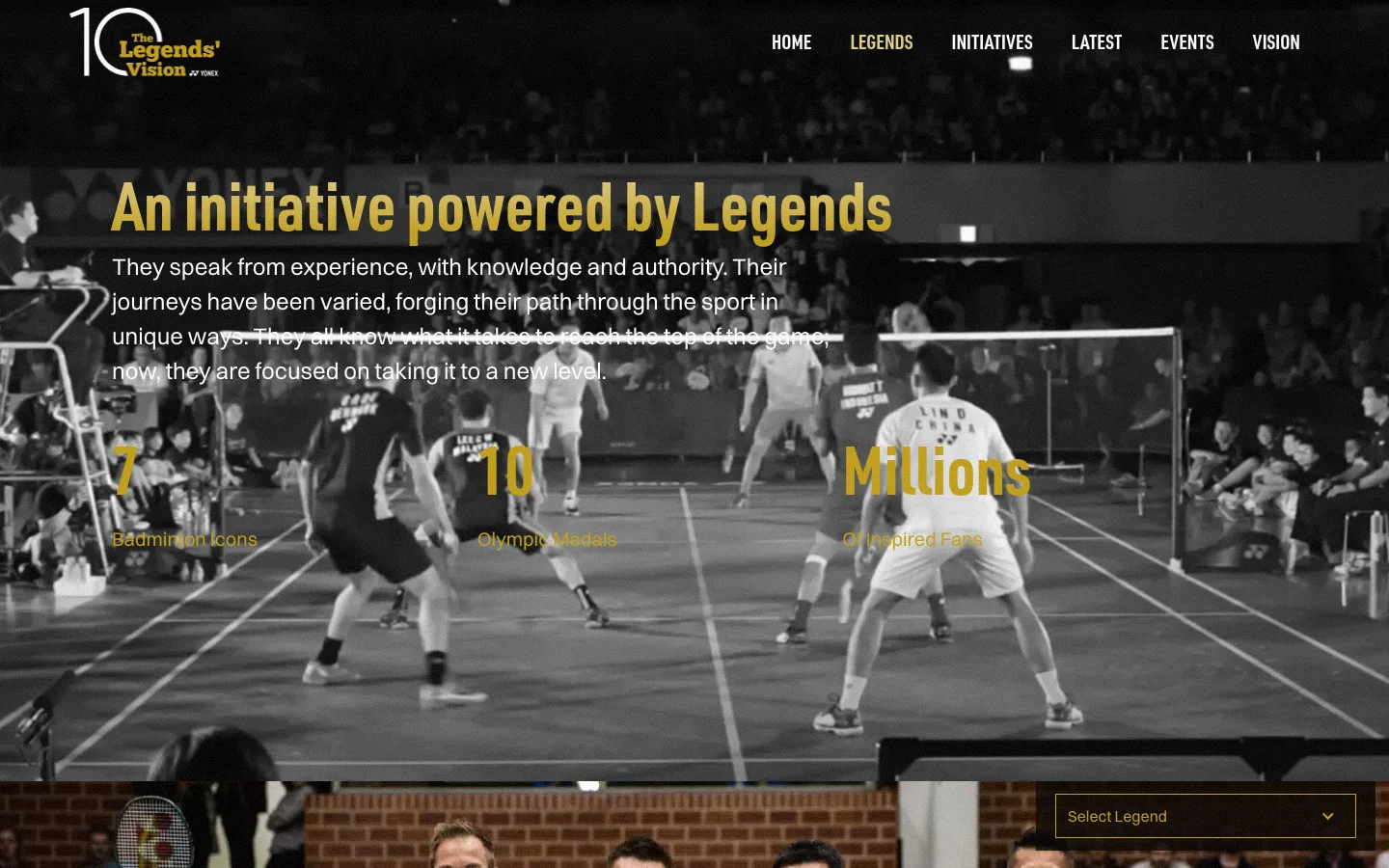 The desktop website features a dark, cinematic hero section with a black and white background image of badminton players on a court. Large gold and white text displays the headline 'An initiative powered by Legends' alongside statistics for icons, medals, and fans, with a navigation menu at the top right and a 'Select Legend' dropdown at the bottom right.