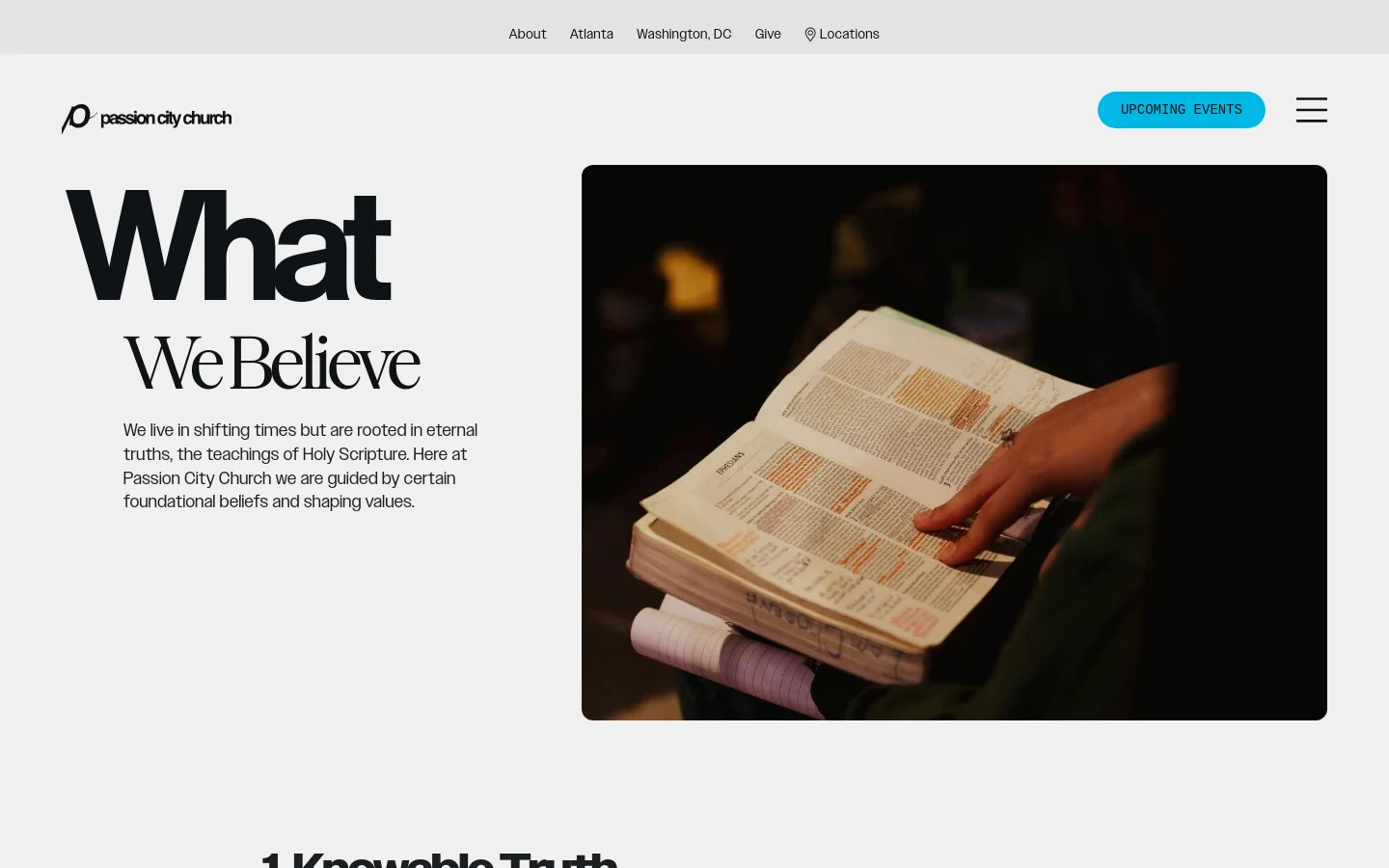The desktop page features a clean white background with a large hero section. On the left, the headline 'What We Believe' is displayed in bold black text above a brief introductory paragraph, while the right side shows a large photograph of hands holding an open Bible. The navigation bar includes the Passion City Church logo, an 'Upcoming Events' button, and a hamburger menu icon.