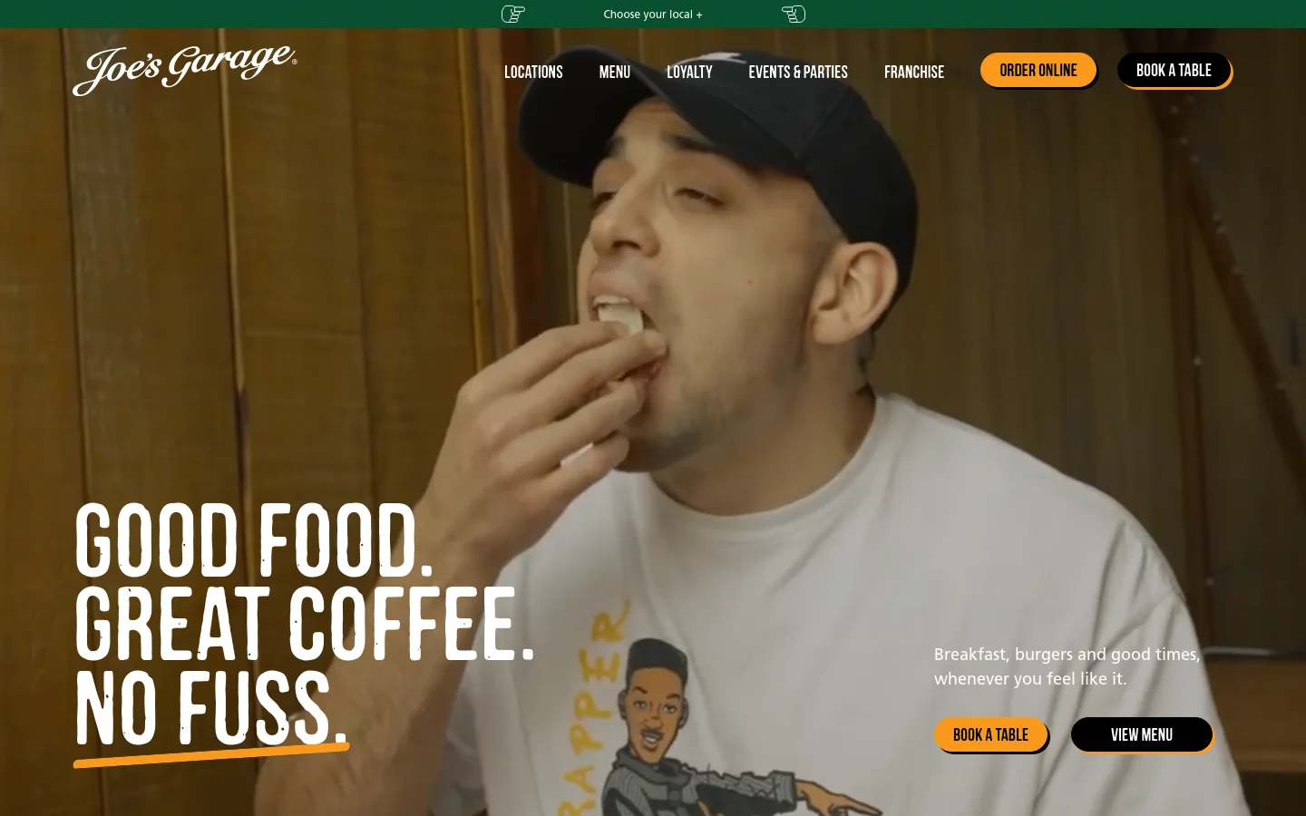 The desktop homepage features a large hero image of a man eating, overlaid with the bold white headline 'GOOD FOOD. GREAT COFFEE. NO FUSS.' A navigation bar at the top includes links for Locations, Menu, and Loyalty, alongside orange and black buttons for 'Order Online' and 'Book a Table'. The layout is spacious with a dark, warm aesthetic.