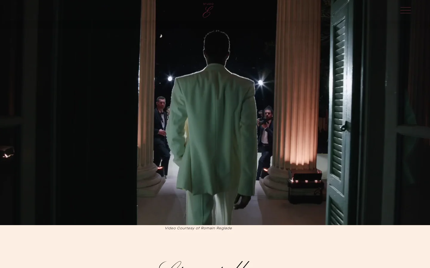 The desktop homepage features a full-screen cinematic video background showing a person in a white suit walking through a grand entrance at night. A minimalist navigation menu and a small pink logo are centered at the top, while a light beige footer contains the text 'Video Courtesy of Romain Reglade' and the headline 'Storytellers'.