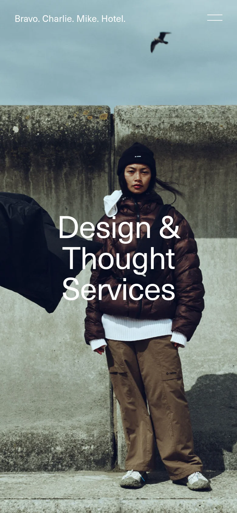 The mobile version maintains the large hero image of two people in winter gear, but the layout is vertically oriented. The navigation links are condensed into a hamburger menu icon in the top right, while the agency name and 'Design & Thought Services' headline are prominently centered over the image.