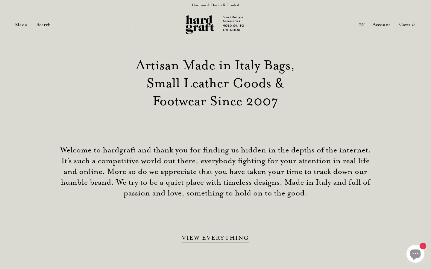 The desktop homepage features a minimalist, light grey background with centered black serif typography. A large headline announces artisan-made Italian goods, followed by a welcoming brand paragraph and a 'VIEW EVERYTHING' call to action link. The navigation bar includes a menu, search, logo, language selector, account, and cart.