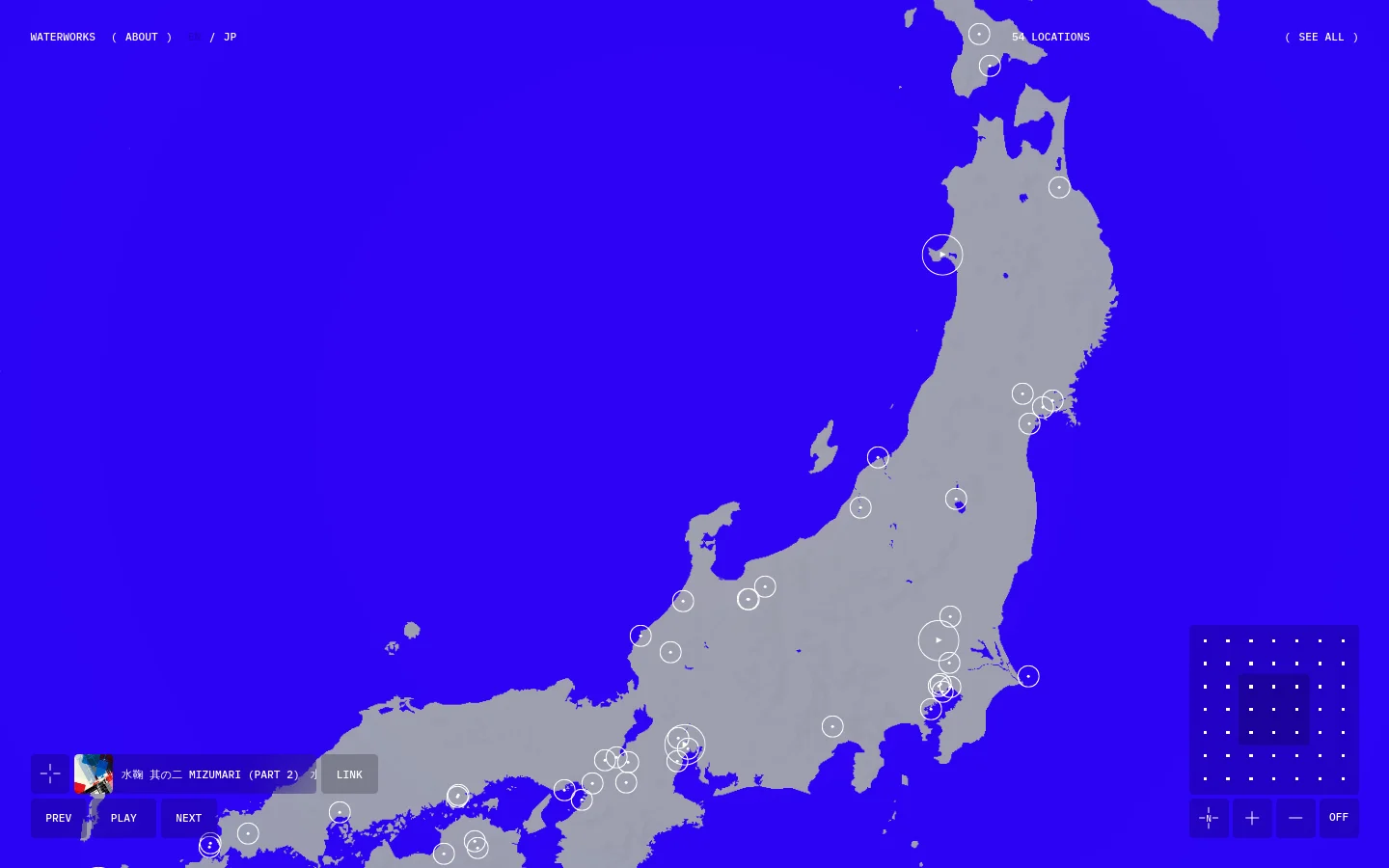 A minimalist website featuring a large gray map of Japan set against a vibrant blue background. White circles of varying sizes are scattered across the map to indicate locations, and navigation links like 'WATERWORKS', 'ABOUT', and '54 LOCATIONS' are displayed in a white monospaced font at the top. Control buttons for zooming and playback are located in the bottom corners.