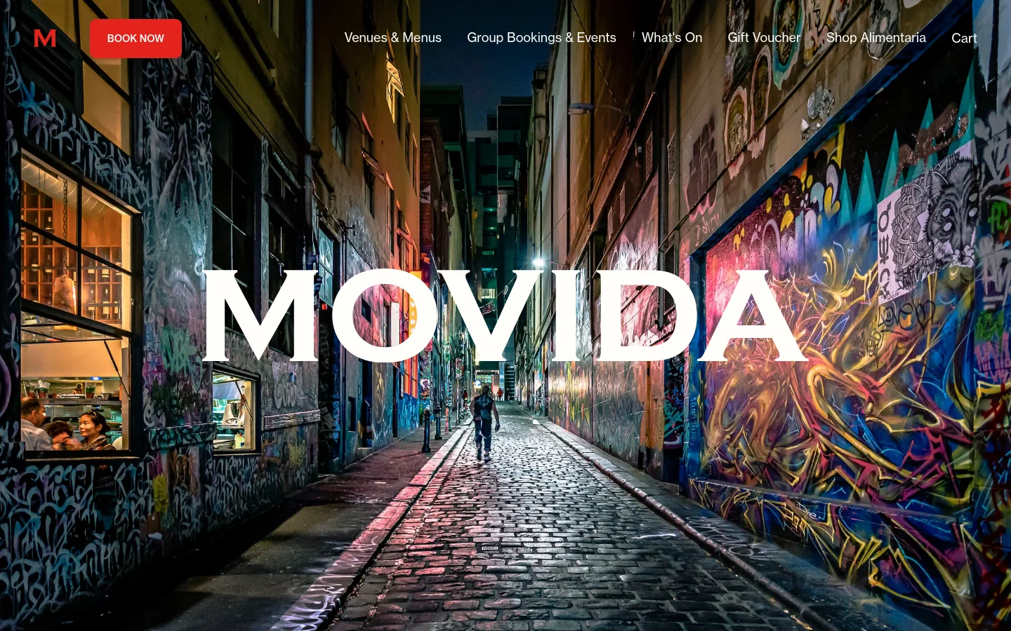 The desktop homepage features a large hero image of a colorful, graffiti-filled Melbourne laneway with the word 'MOVIDA' in bold white text centered. A red 'BOOK NOW' button is prominent in the top left, next to a navigation menu including Venues & Menus, Group Bookings & Events, What's On, Gift Voucher, Shop Alimentaria, and Cart.