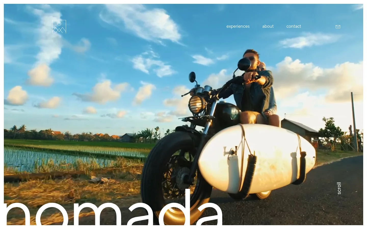 The desktop homepage features a large hero image of a person riding a motorcycle with a surfboard attached, set against a bright sky and rice fields. A minimalist navigation menu with links for experiences, about, and contact sits at the top right, above the large white 'nomada' wordmark at the bottom. The layout is clean with a wide-screen focus and a vertical 'scroll' indicator on the right.
