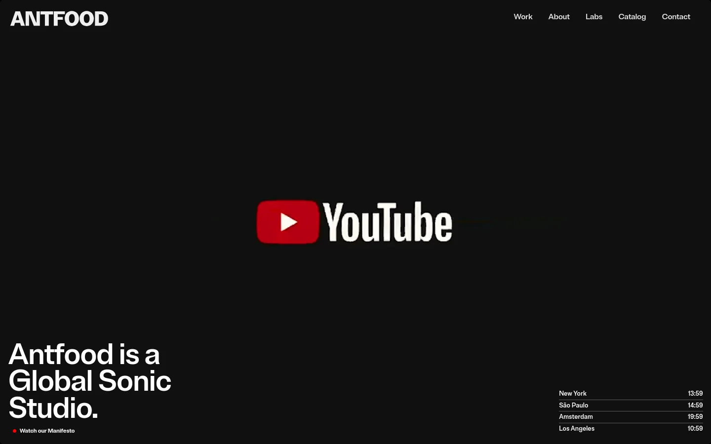 The desktop homepage features a dark, minimalist aesthetic with a large video player centered on the screen and the headline 'Antfood is a Global Sonic Studio' in the bottom left. A navigation menu is at the top right, and the bottom right displays global time zones for New York, São Paulo, Amsterdam, and Los Angeles. A 'Watch our Manifesto' call to action is positioned near the bottom left.