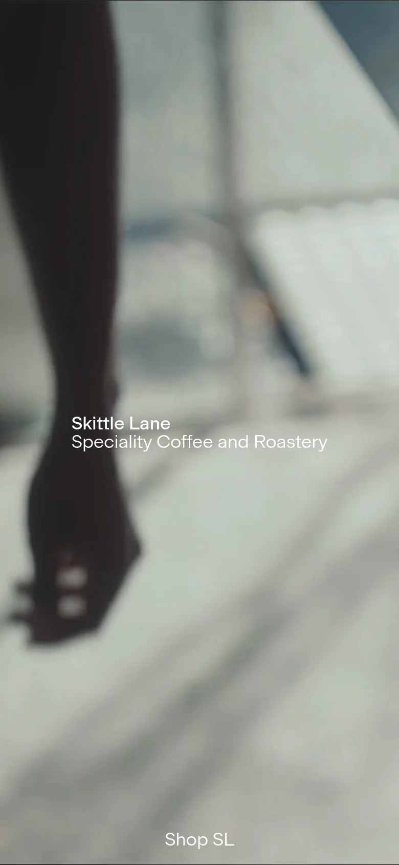 The mobile version presents a vertically oriented, zoomed-in version of the roastery hero image, focusing on a blurred foreground element. The white text 'Skittle Lane Speciality Coffee and Roastery' and the 'Shop SL' button are stacked vertically in the center of the screen.