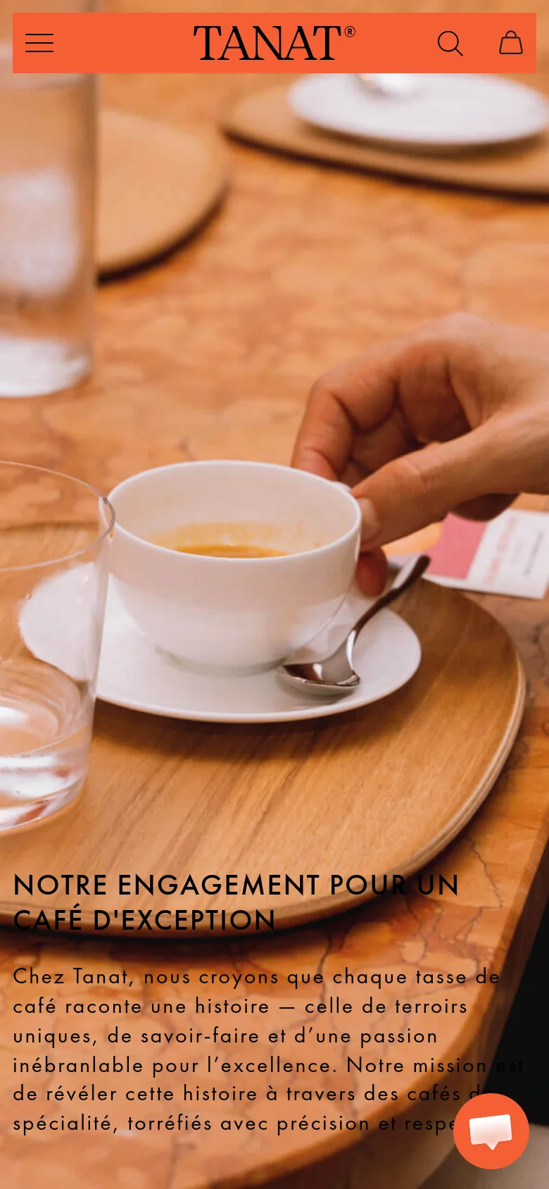 The mobile version presents a vertically oriented view of the same warm-toned hero image, focusing closely on the coffee cup and hand. The navigation is condensed into a hamburger menu icon on the left, with a search icon and shopping bag on the right. The headline and mission statement are stacked vertically at the bottom of the screen, accompanied by a floating orange chat icon in the corner.