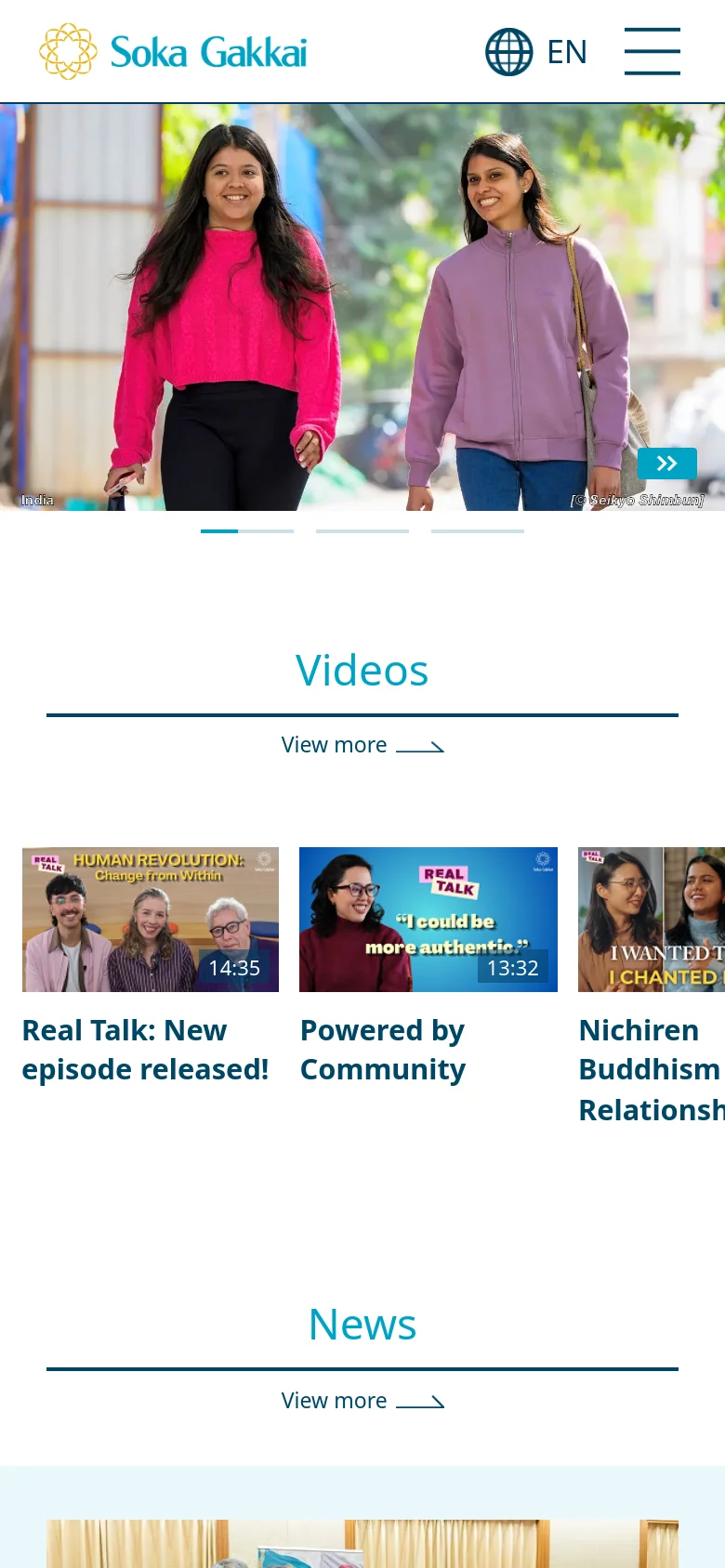 The mobile version features a condensed header with the Soka Gakkai logo, an 'EN' language selector, and a hamburger menu icon. The hero image of two smiling women is scaled to fit the vertical screen, followed by a 'Videos' section with horizontally arranged video thumbnails and a 'View more' link.