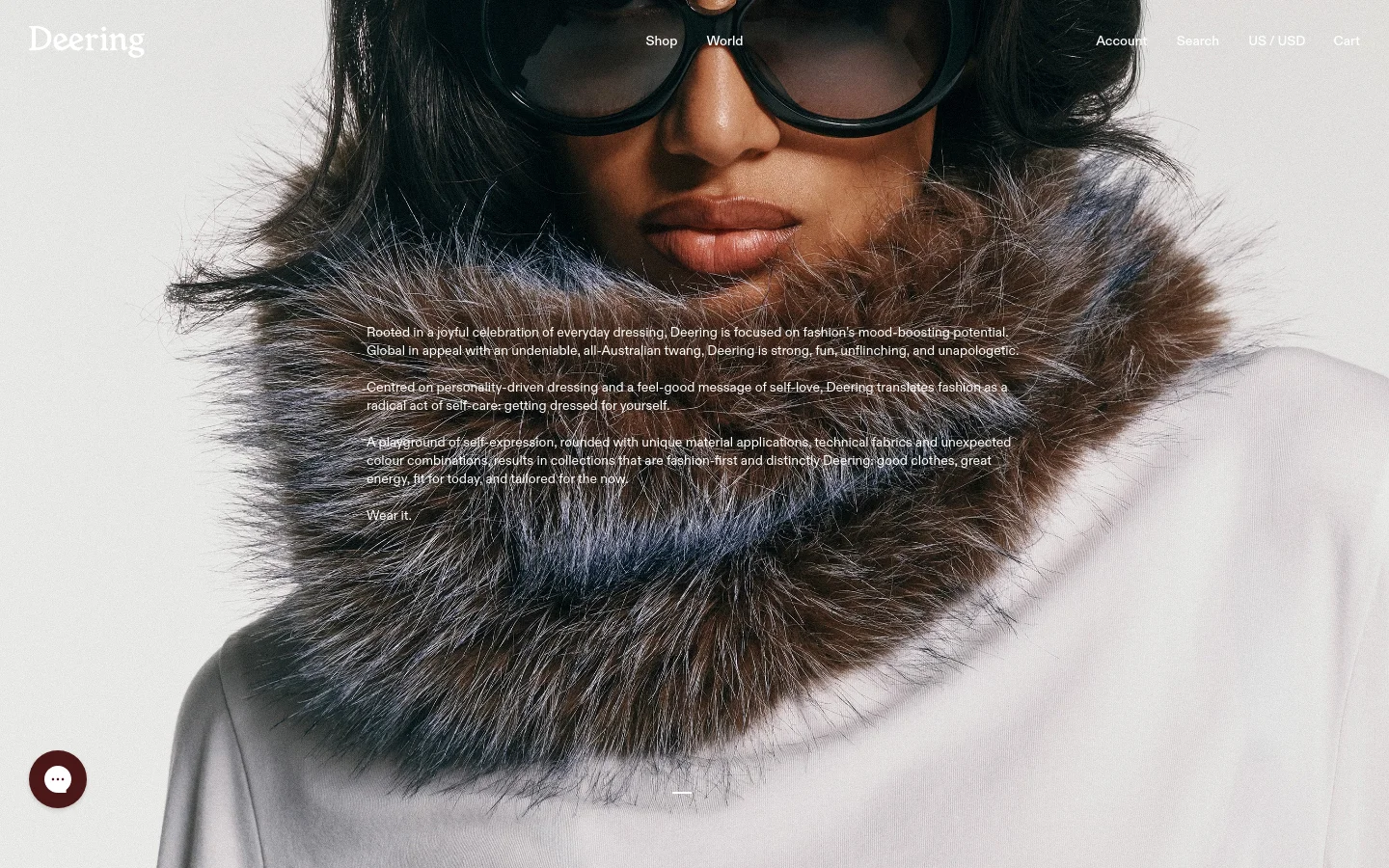 The desktop About page features a large, high-fashion hero image of a person wearing dark sunglasses and a voluminous faux-fur collar. White text overlays the center of the image, detailing the brand's philosophy, while the navigation menu is spread across the top with links for Shop, World, Account, Search, and Cart.