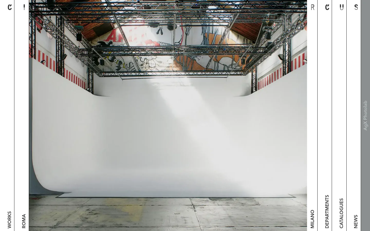 The desktop homepage features a minimalist, high-fashion aesthetic with a large hero image of a bright white photography studio cyclorama. The layout uses thin vertical lines to divide the screen into columns, with text labels like 'WORKS', 'ROMA', 'MILANO', and 'DEPARTMENTS' oriented vertically along the edges.
