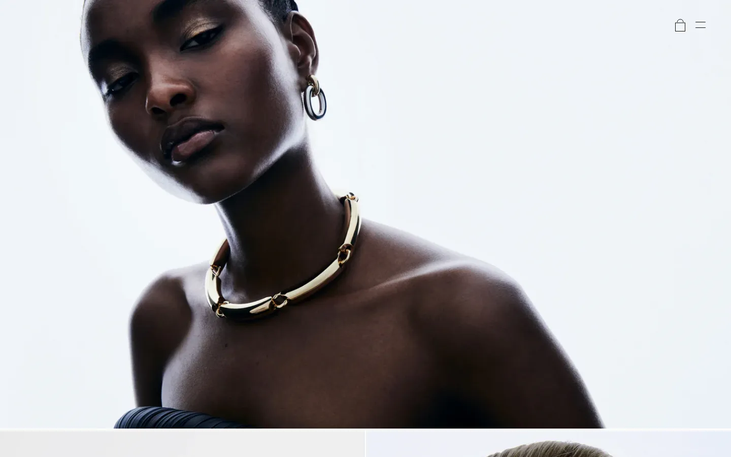 The desktop homepage features a minimalist design with a large, high-contrast hero image of a model wearing a gold link necklace against a white background. Below the hero section, a clean grid layout displays various jewelry products like earrings and bracelets with their names and prices. The color palette is neutral, focusing on black, white, and metallic tones.