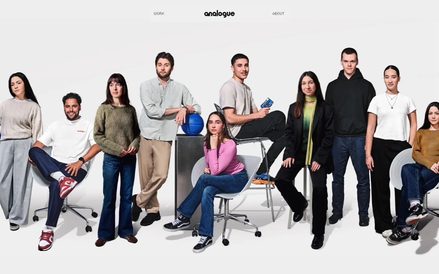 Analogue Agency team page featuring a large group portrait of diverse staff members against a light grey background. The minimalist layout uses a centered logo with WORK and ABOUT navigation links above a full-bleed hero image of the team in casual attire.