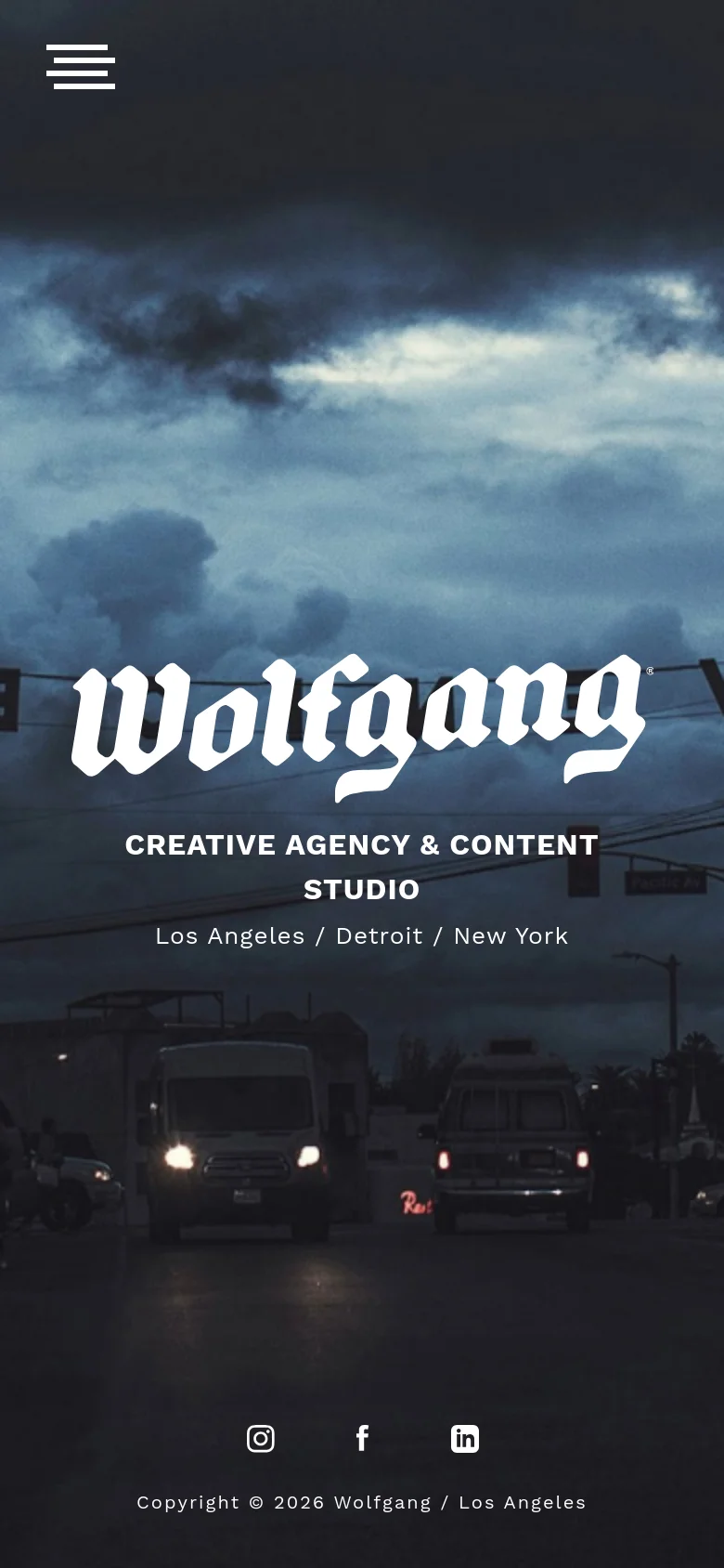 The mobile version presents a vertically oriented hero image of a dark, cloudy sky over a street scene with vehicles. The 'Wolfgang' logo and agency description are centered in white text, and the layout is simplified with social media icons and copyright information positioned at the bottom of the screen.