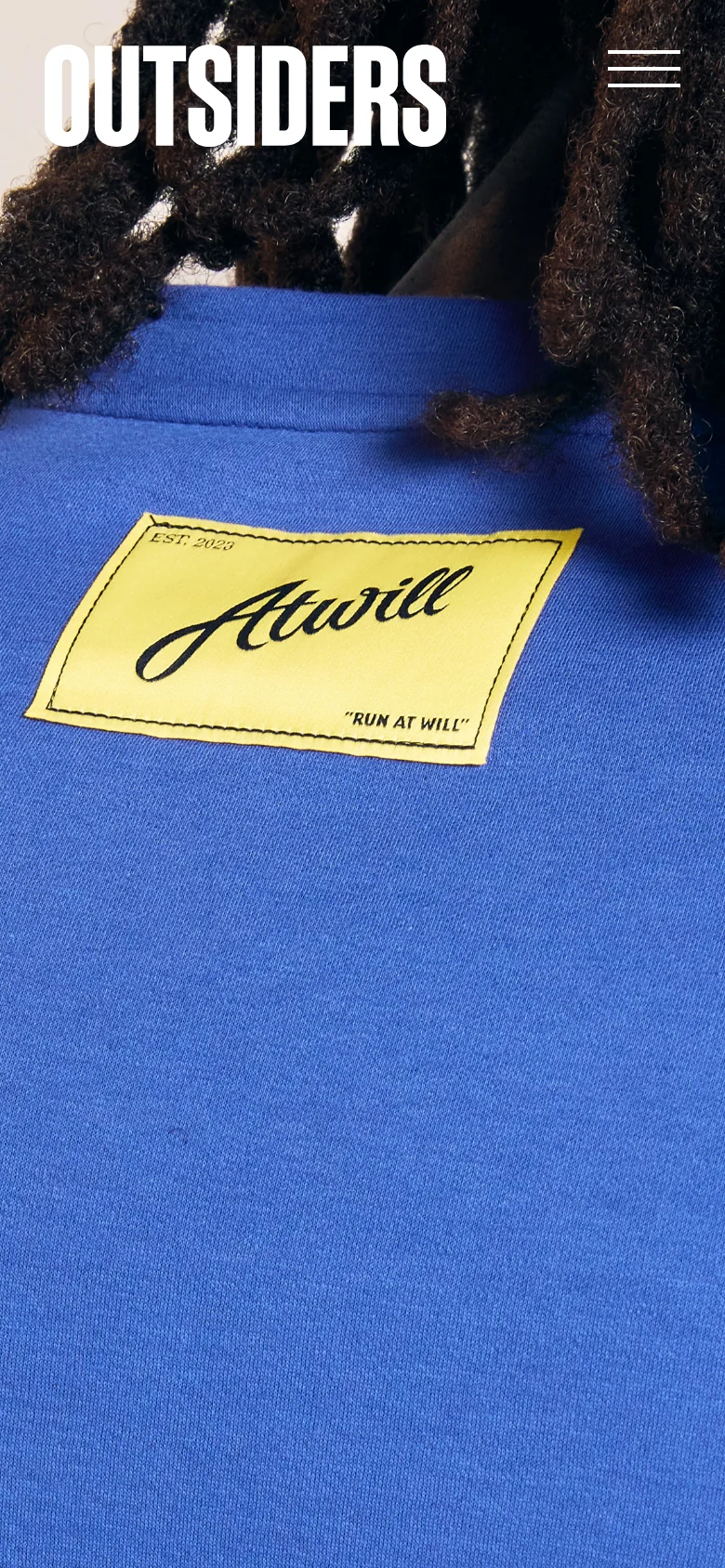 The mobile version shows a full-screen hero image of a blue garment with a yellow 'Atwill' label. The white 'OUTSIDERS' logo is positioned prominently in the upper left, with a three-line hamburger menu icon in the upper right.