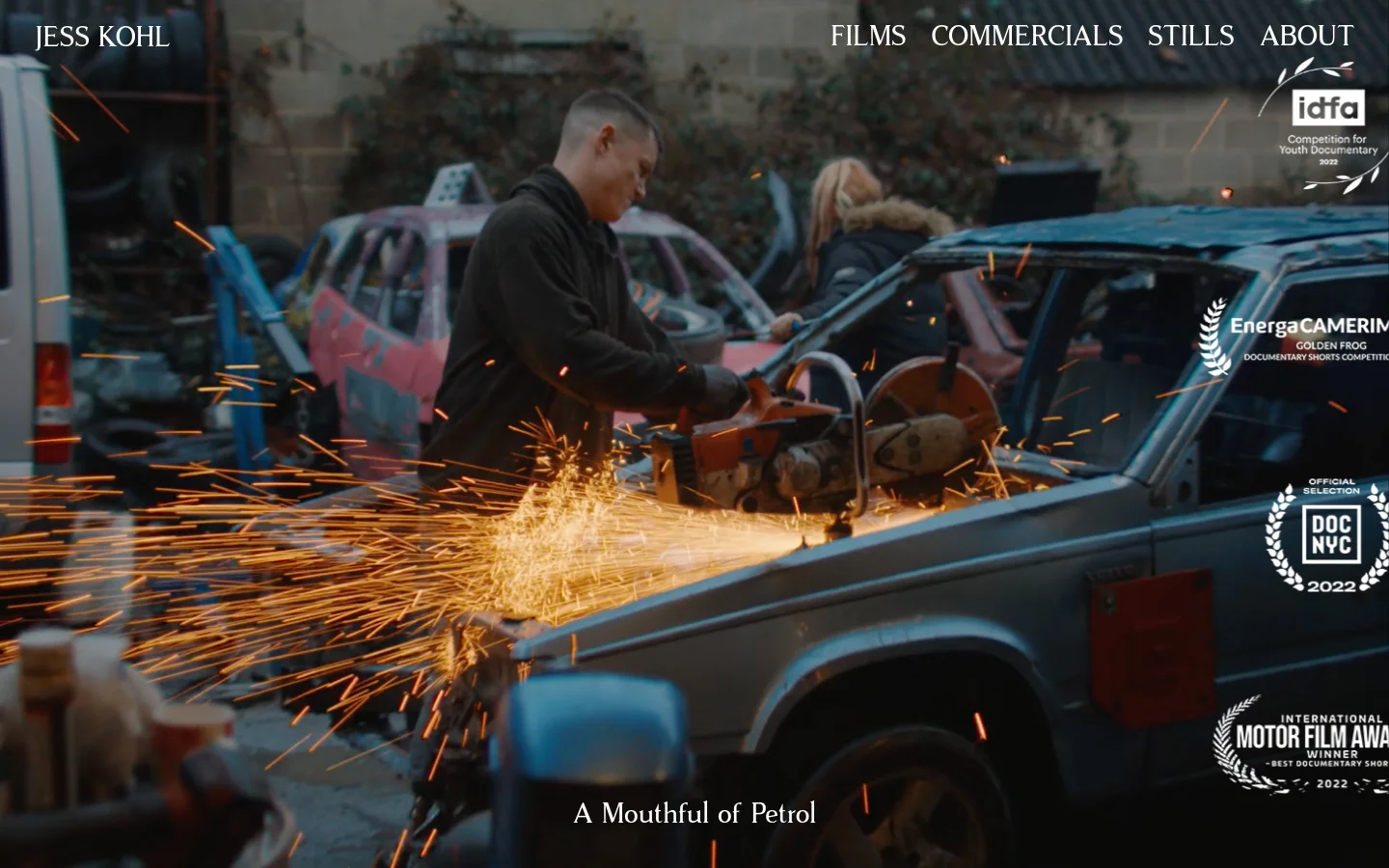 The desktop version features a full-screen cinematic hero image of a man using a power tool on a car, creating bright orange sparks. The title 'A Mouthful of Petrol' is at the bottom, and navigation links for Films, Commercials, Stills, and About are in the top right. Various film award laurels are overlaid on the right side of the image.