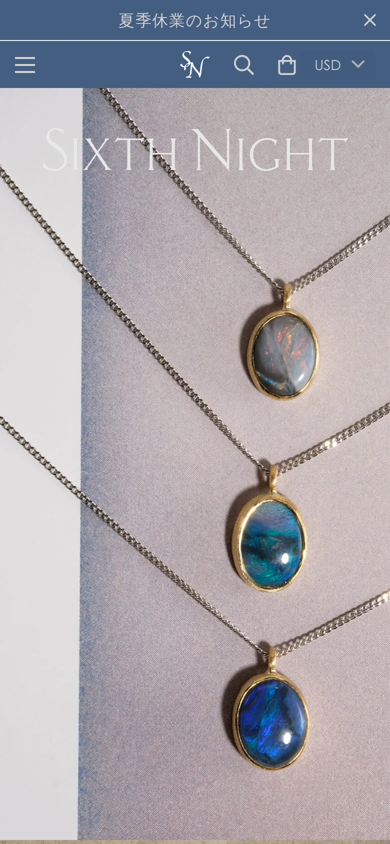 The mobile version shows the same hero image of layered gemstone necklaces, but the navigation is condensed into a hamburger menu icon on the left. The brand logo is centered, with search and shopping bag icons to the right. A prominent blue announcement bar with Japanese text and a close button sits at the top of the screen.