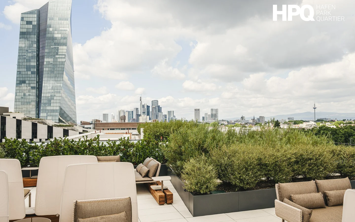 The desktop page features a large hero image of a modern rooftop terrace with lounge seating, lush greenery, and a view of the Frankfurt skyline under a cloudy sky. Below, the layout uses a clean white background with dark text, organized into sections with headlines and descriptive text interspersed with large, high-quality images of landscaped courtyards and luxury interiors. The color palette is sophisticated, utilizing neutrals, greens, and blues.