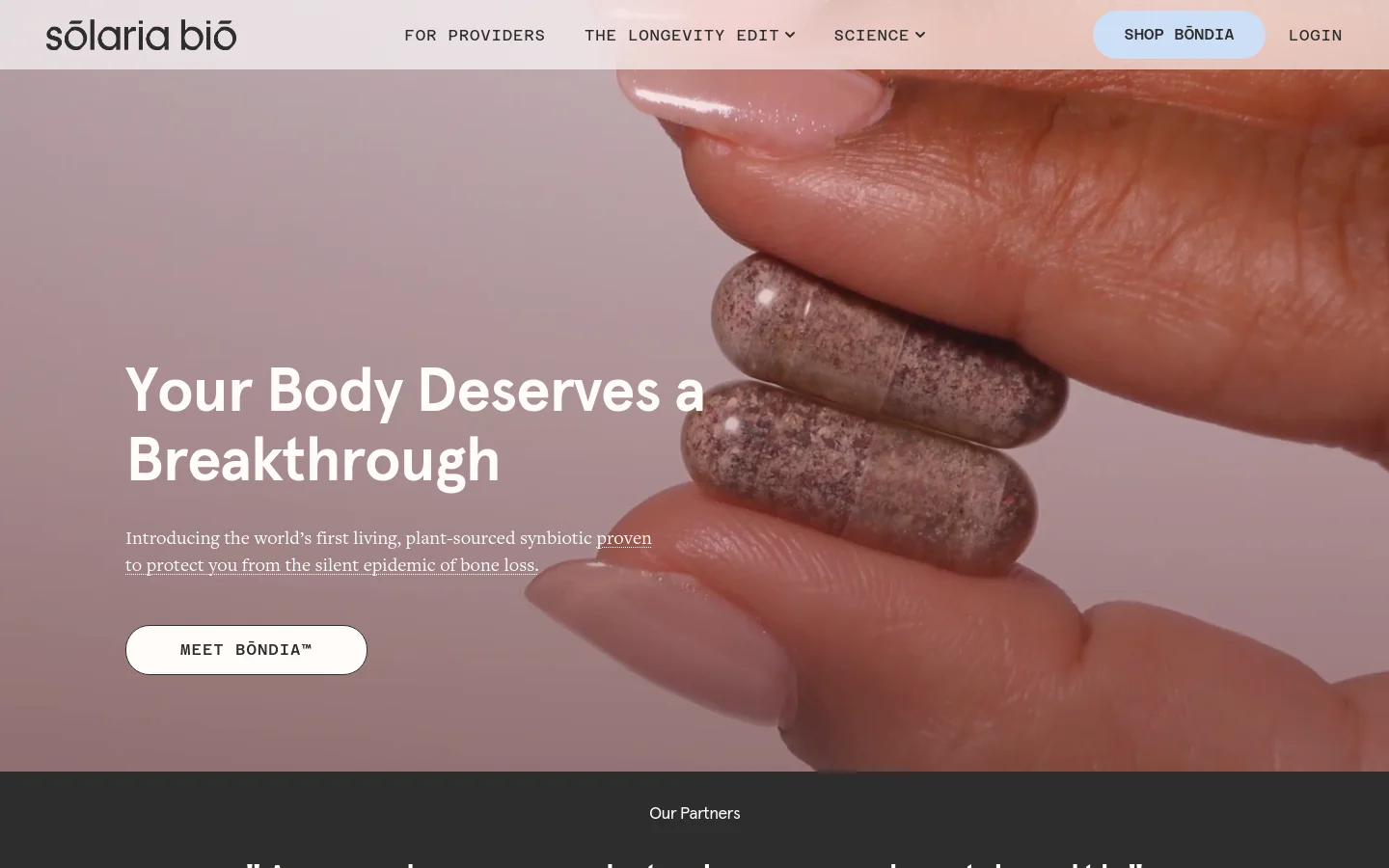 The desktop homepage features a large hero image of fingers holding two speckled capsules against a soft pink background. The headline reads 'Your Body Deserves a Breakthrough' with a white 'MEET BŌNDIA™' call-to-action button. A navigation bar at the top includes links for providers, science, and a 'SHOP BŌNDIA' button.