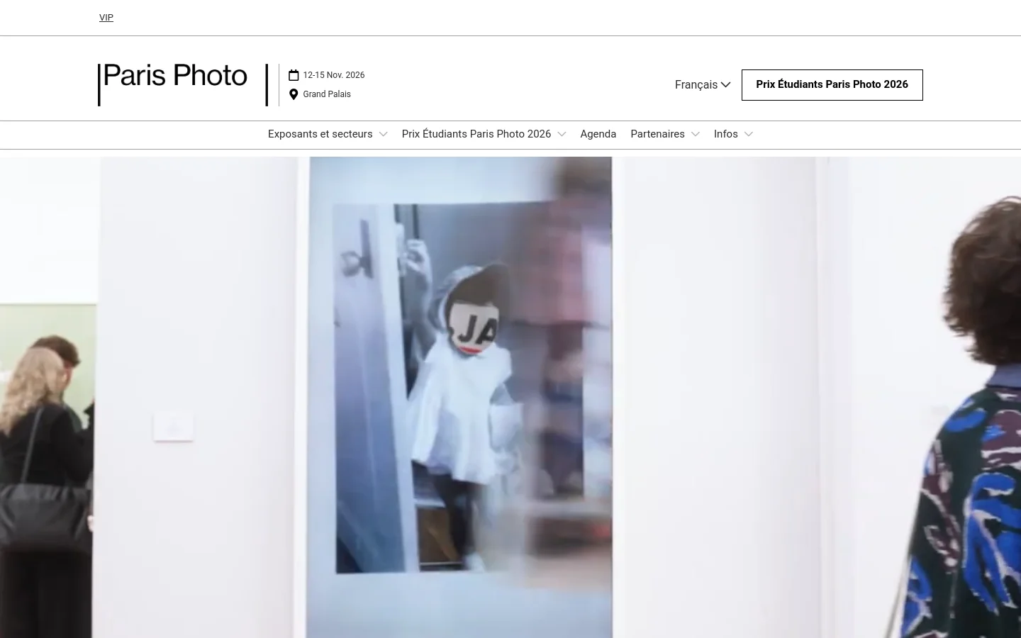 The desktop homepage features a minimalist white header with the Paris Photo logo, event dates, and location. A navigation menu includes dropdowns for exhibitors, awards, agenda, partners, and info, alongside a prominent button for the Paris Photo Student Prize. The hero section displays a large, soft-focus photograph of people in an art gallery setting.