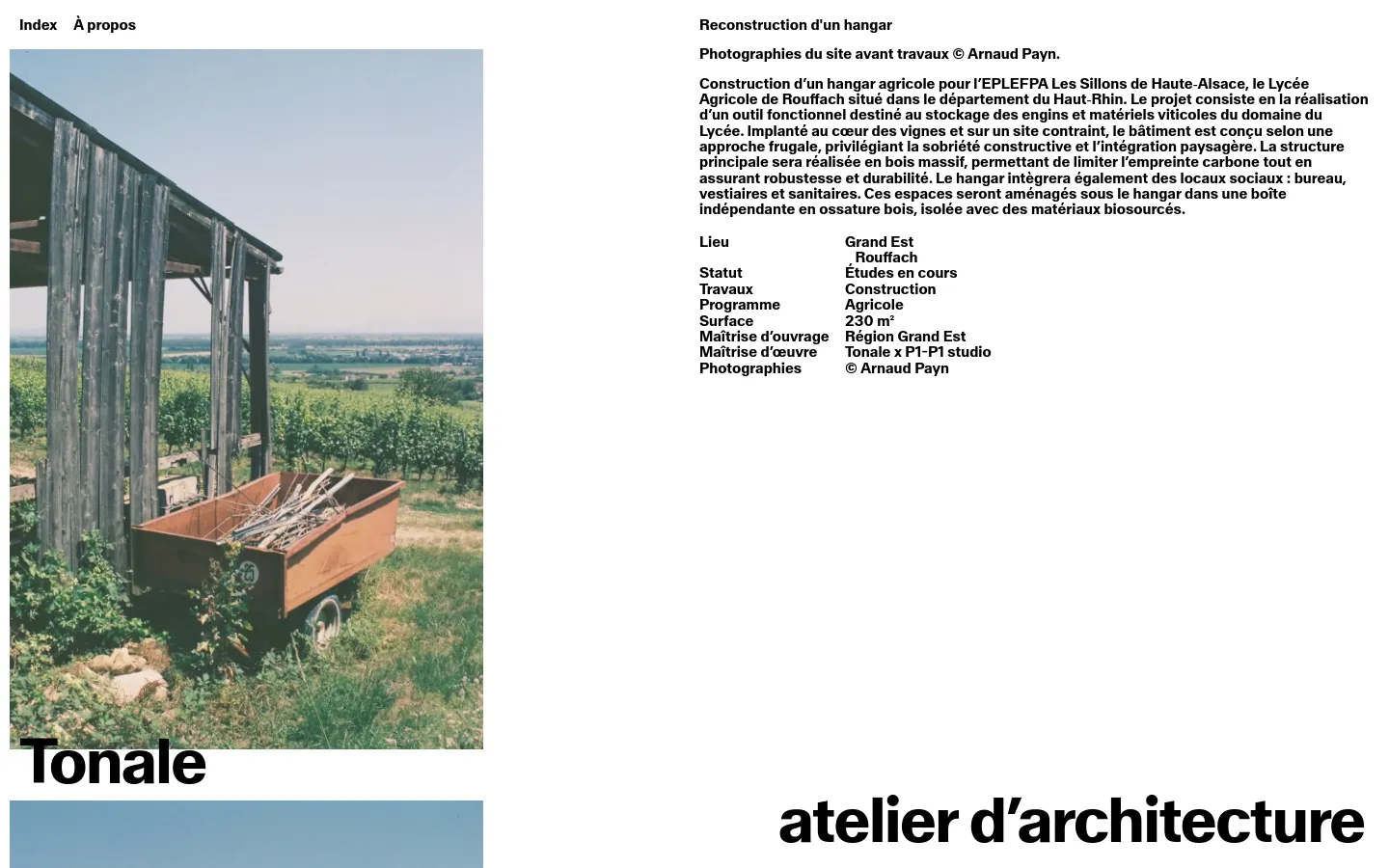The desktop page features a minimalist design with a large landscape photograph of a rural site with vineyards and a wooden structure on the left. To the right, the project title 'Reconstruction d'un hangar' is followed by descriptive text and a structured list of project details like location, status, and surface area. The layout uses a clean white background with black typography and a navigation menu at the top.