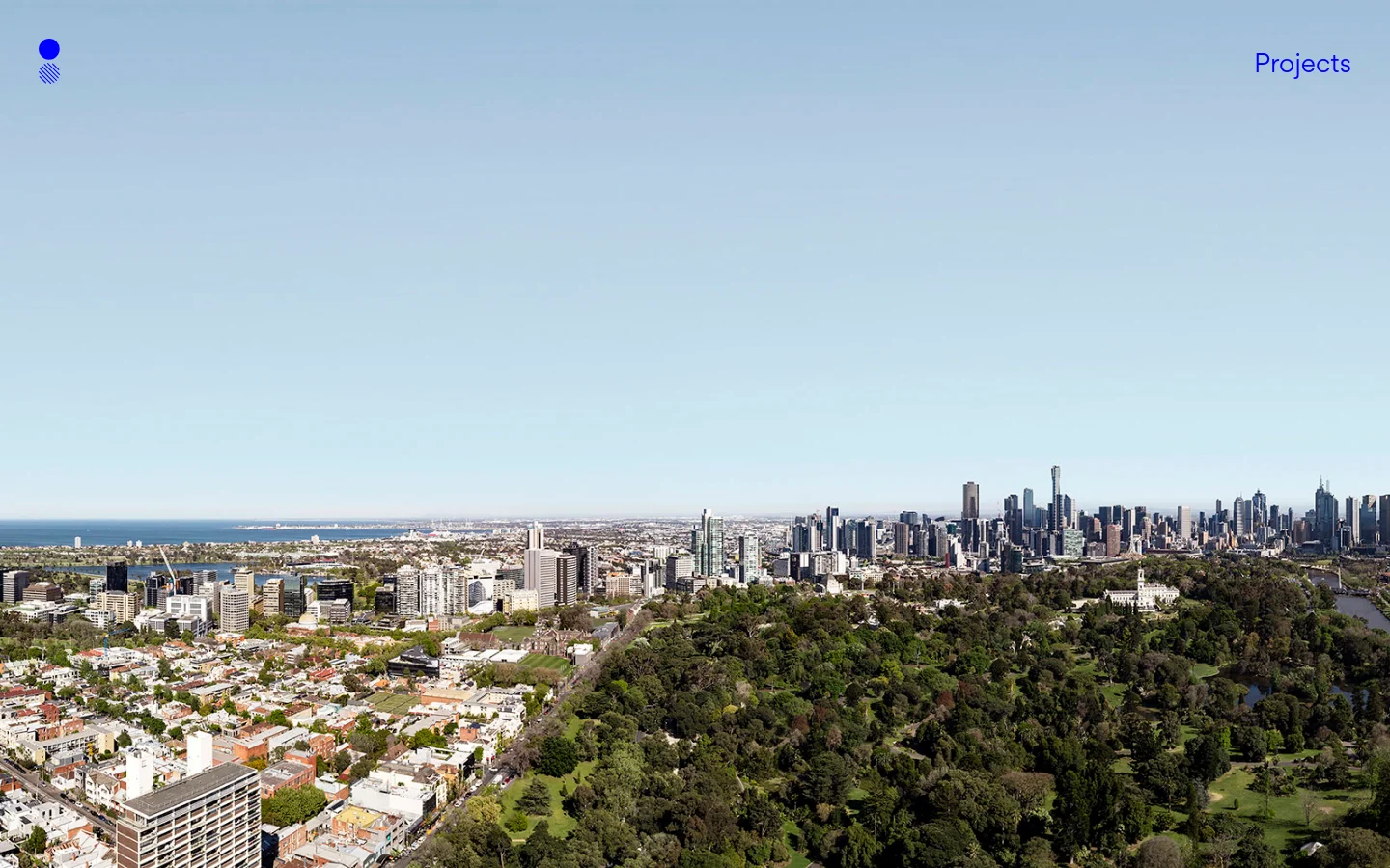 The desktop homepage features a minimalist design with a large, high-resolution panoramic hero image of a city skyline overlooking lush green parks and residential areas under a clear blue sky. A small blue circular logo is in the top left, and a 'Projects' navigation link is in the top right, set against a vast, light blue sky background.