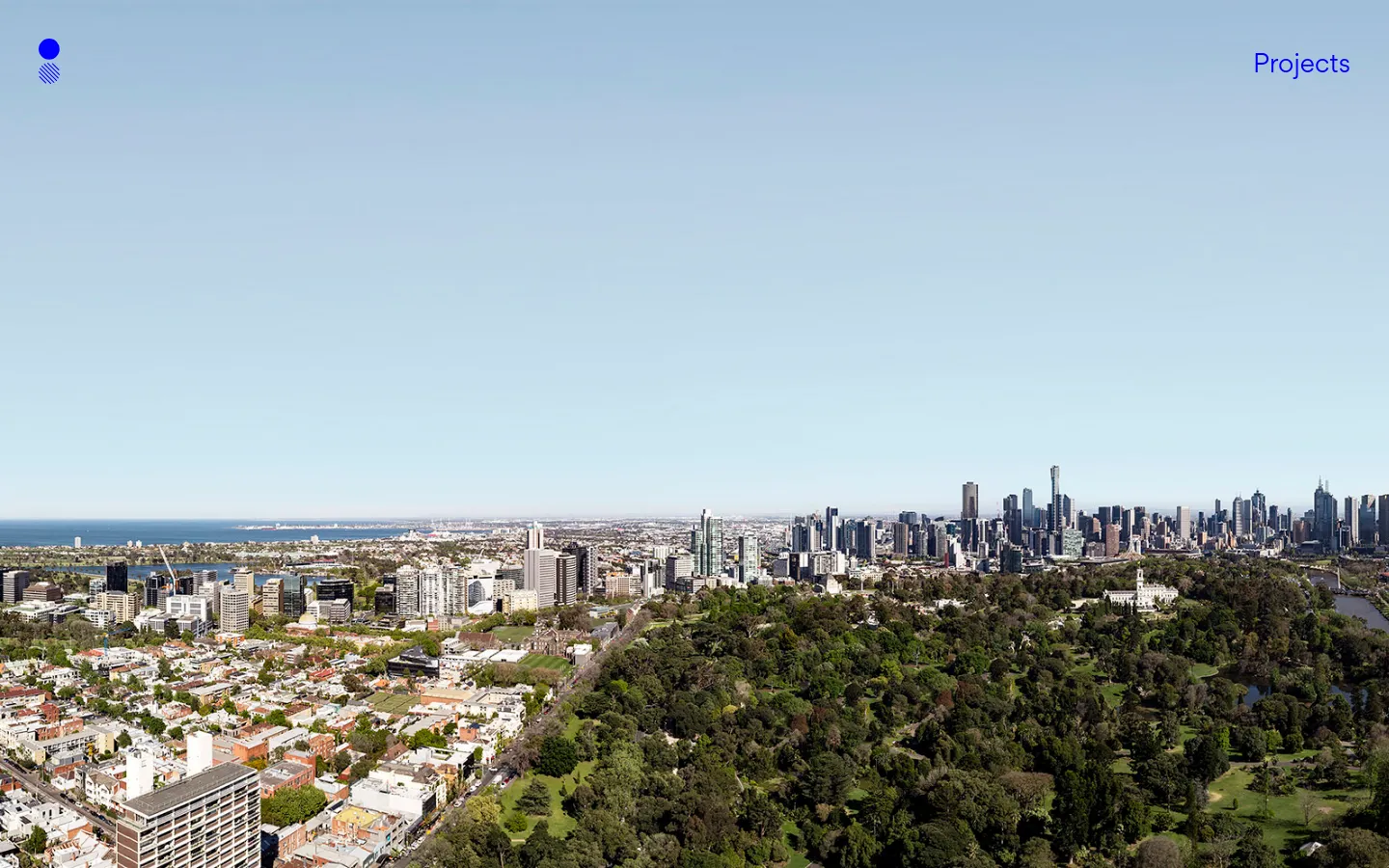 The desktop homepage features a minimalist design with a large, high-resolution panoramic hero image of a city skyline overlooking lush green parks and residential areas under a clear blue sky. A small blue circular logo is in the top left, and a 'Projects' navigation link is in the top right, set against a vast, light blue sky background.