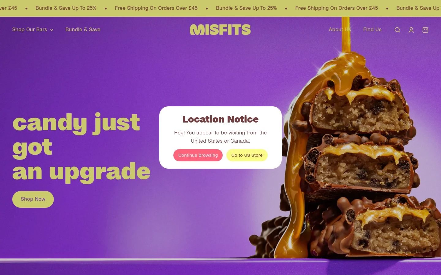 Desktop homepage for Misfits featuring a vibrant purple background with a large hero image of stacked chocolate protein bars dripping with caramel. A large headline reads 'candy just got an upgrade' next to a lime green 'Shop Now' button, while a central 'Location Notice' pop-up overlay appears. The navigation bar includes the Misfits logo, 'Shop Our Bars', 'Bundle & Save', 'About Us', and 'Find Us'.
