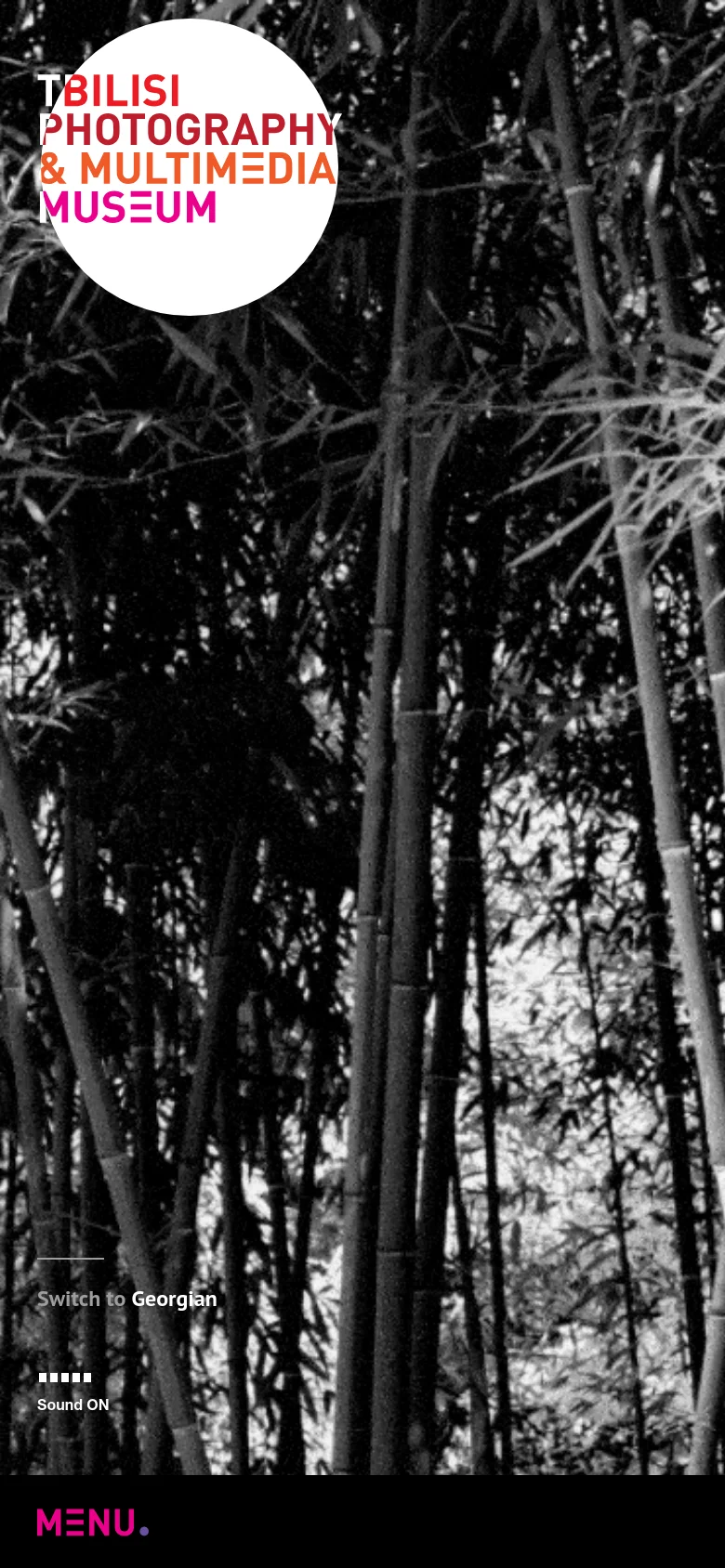 The mobile version presents a full-screen, high-contrast black and white photographic background of dense bamboo stalks. The museum's name is overlaid in large, bold pink and white text within a white circular shape in the upper-left corner. Navigation is simplified with a prominent 'MENU' call to action at the bottom left.