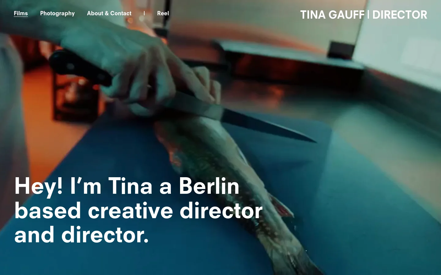 The desktop homepage features a large cinematic hero image of hands preparing food with a knife, overlaid with the white text headline 'Hey! I’m Tina a Berlin based creative director and director.' A minimalist navigation menu at the top includes links for Films, Photography, About & Contact, and Reel, alongside the name 'TINA GAUFF | DIRECTOR' on the right.