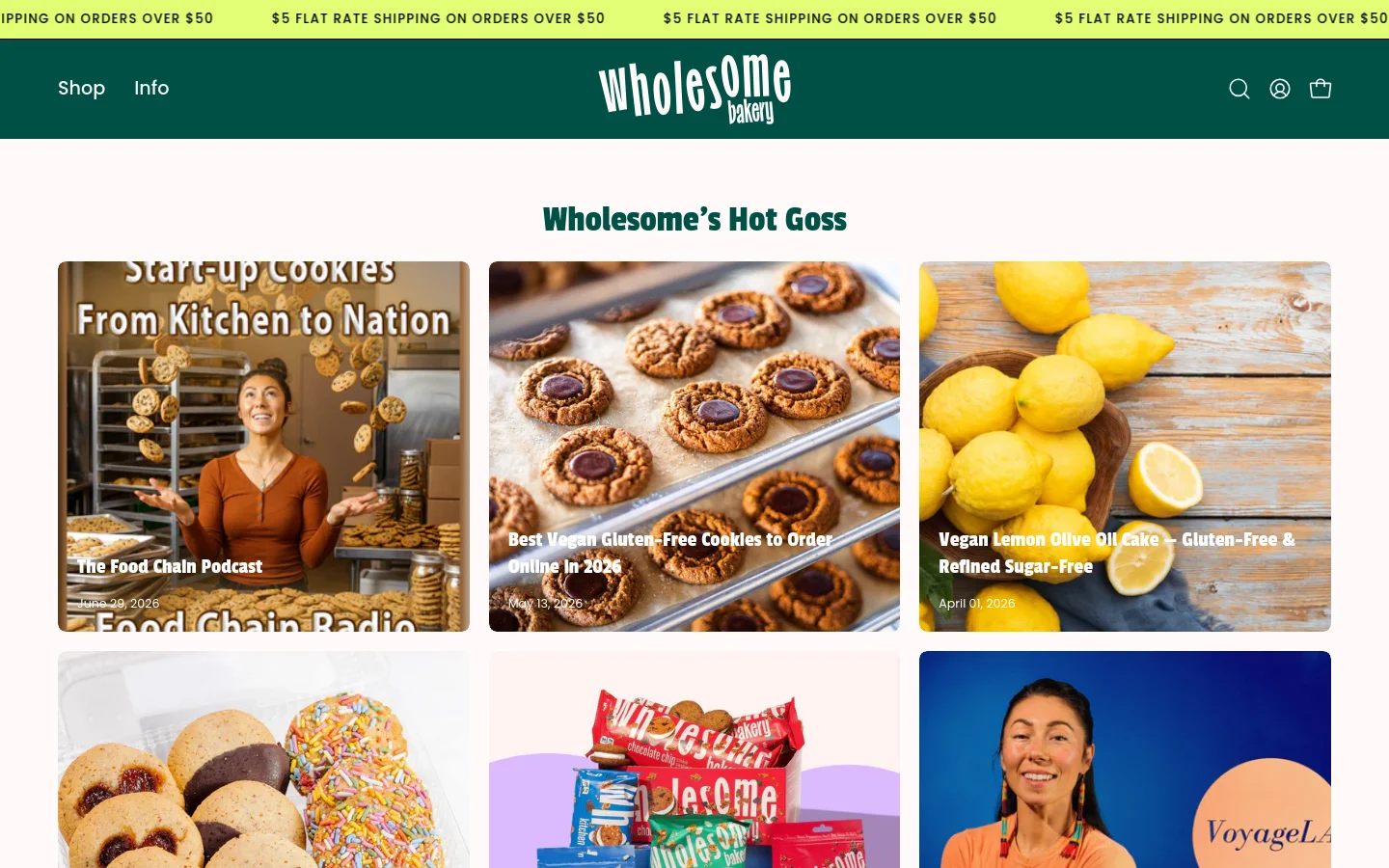 The Wholesome Bakery blog page features a dark green header with the brand logo, search, account, and cart icons. The main content area displays a grid of blog posts under the headline 'Wholesome’s Hot Goss,' each consisting of a large rectangular image with a title and date overlay. The posts shown include a podcast feature, a guide to vegan cookies, and a lemon olive oil cake recipe.