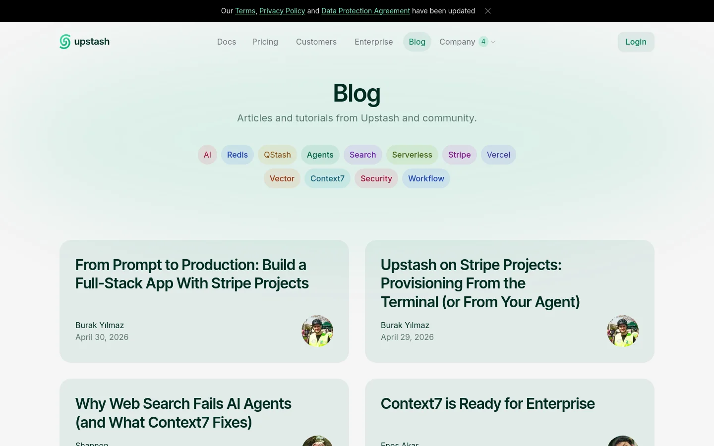 The Upstash blog page features a clean, minimalist design with a light mint green background. A large 'Blog' heading is followed by a subtitle and a horizontal row of pill-shaped category tags like AI, Redis, and QStash. Below, blog posts are arranged in a two-column grid, each displaying a large bold title, author name, date, and a circular author profile image.
