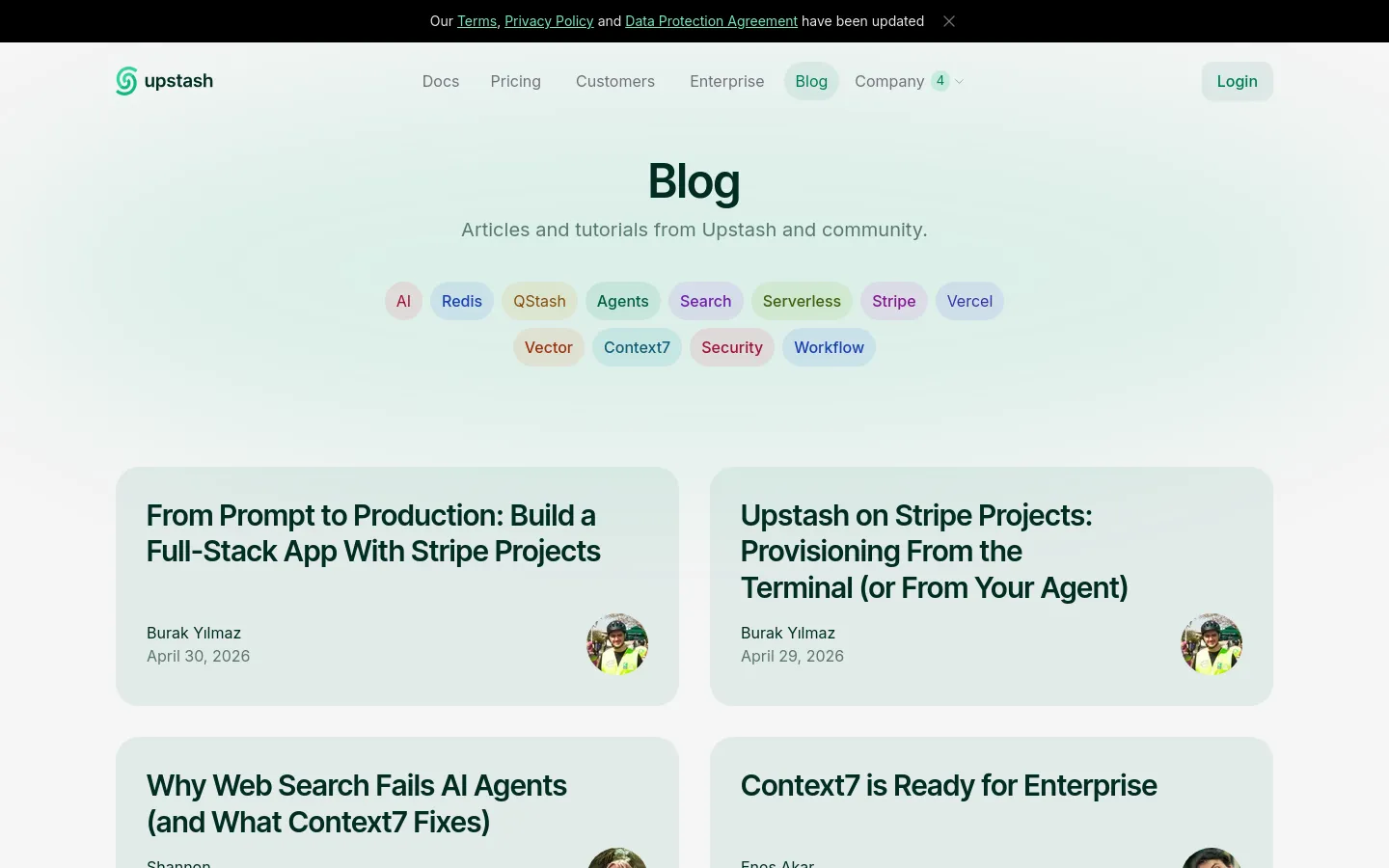 The Upstash blog page features a clean, minimalist design with a light mint green background. A large 'Blog' heading is followed by a subtitle and a horizontal row of pill-shaped category tags like AI, Redis, and QStash. Below, blog posts are arranged in a two-column grid, each displaying a large bold title, author name, date, and a circular author profile image.