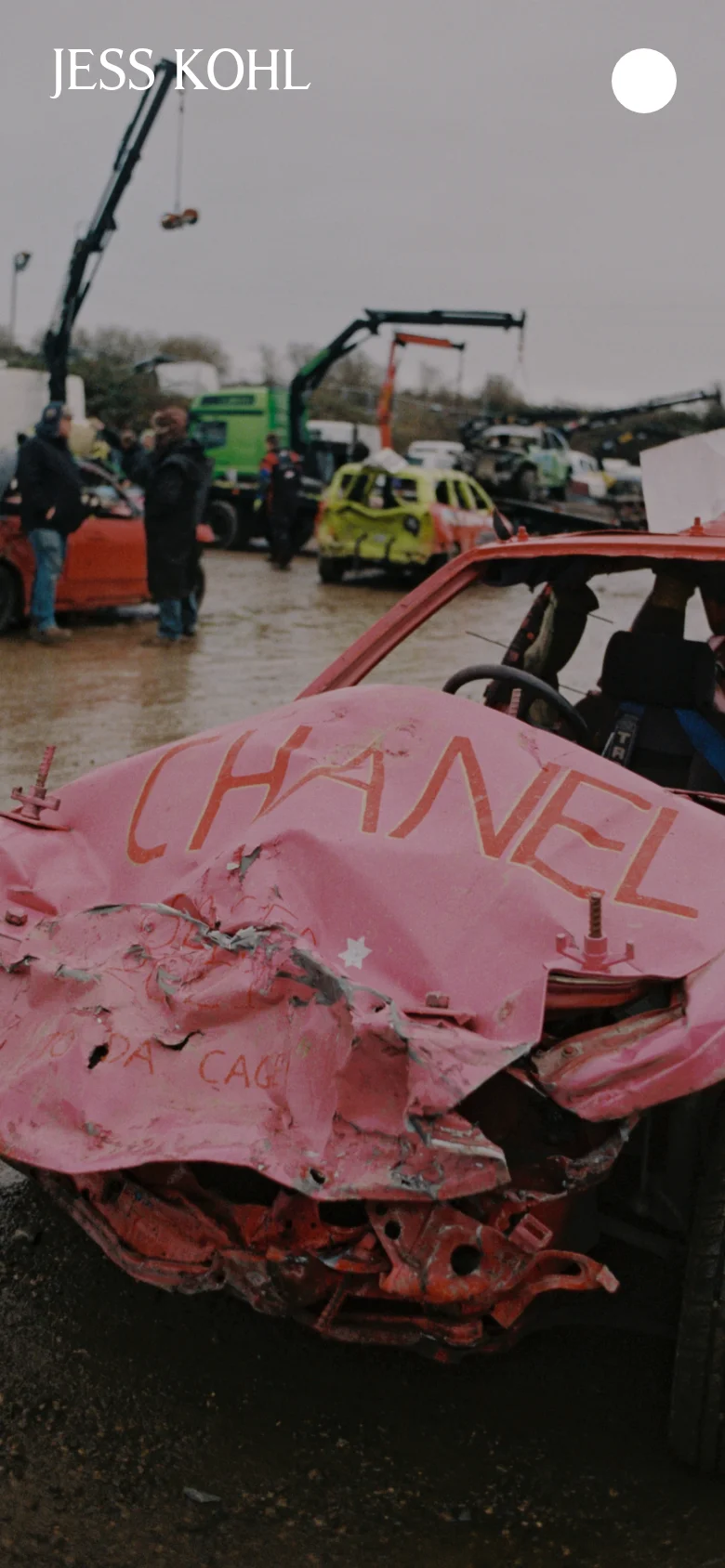 The mobile version displays the same cinematic hero image of the crashed pink car, but the layout is simplified. The navigation menu is replaced by a single white circular icon in the top right, while the name 'JESS KOHL' remains prominently in the top left.